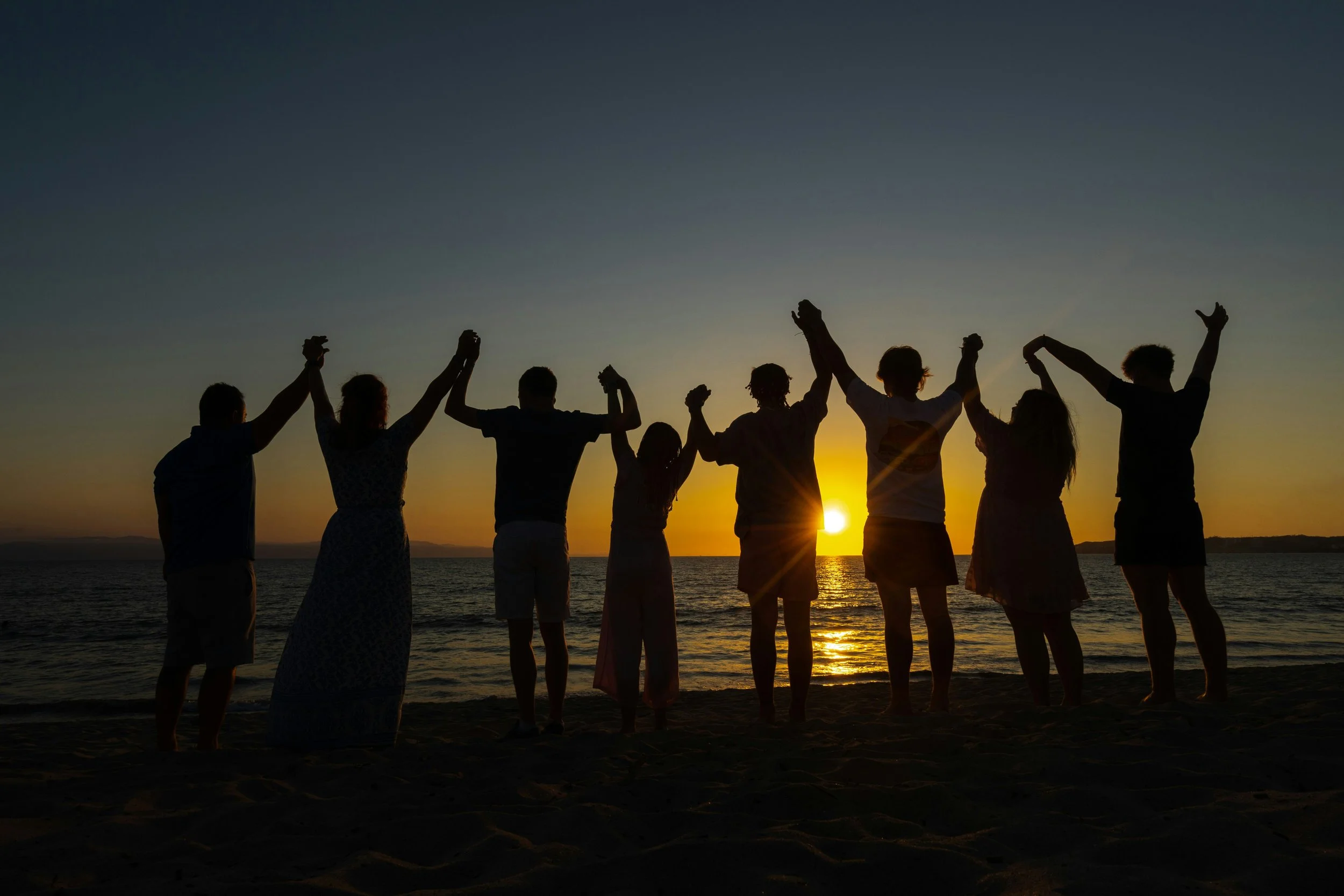 Group of people together at sunset arms spread - healing emotional abandonment and building secure attachment and genuine connection through online therapy with Inese Jegorova UK