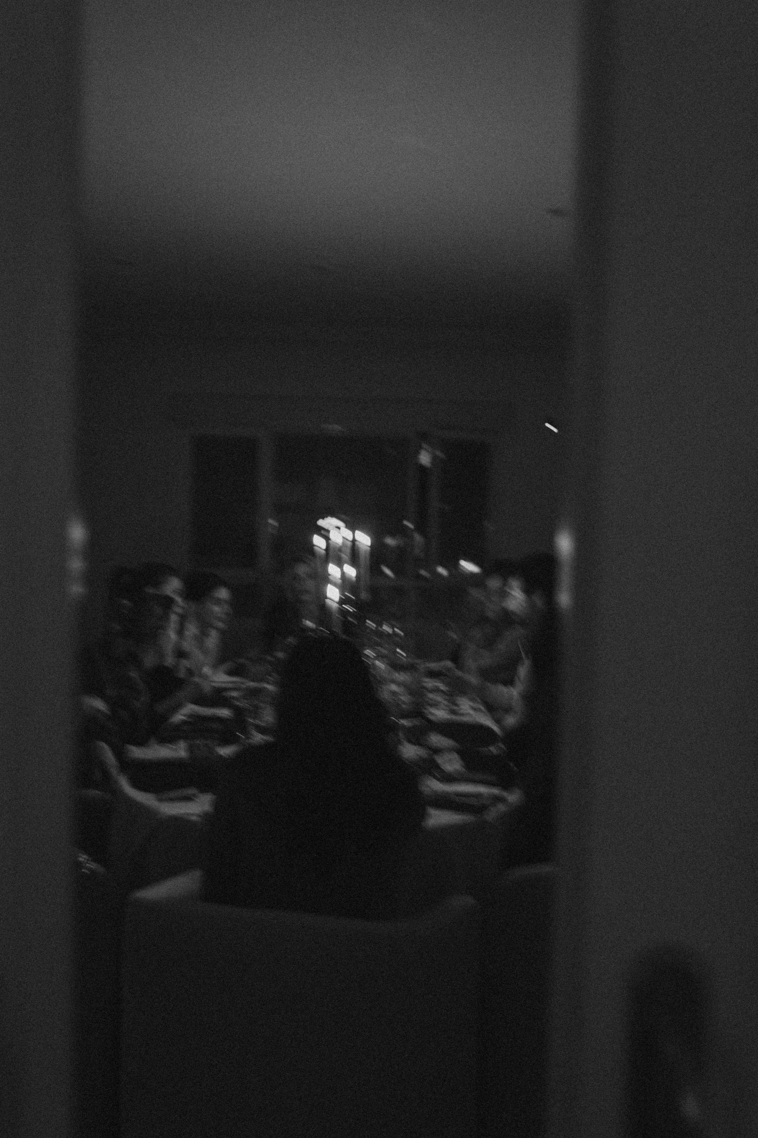 A group of people sitting at tables in a dimly lit room, possibly attending a meeting or a gathering.