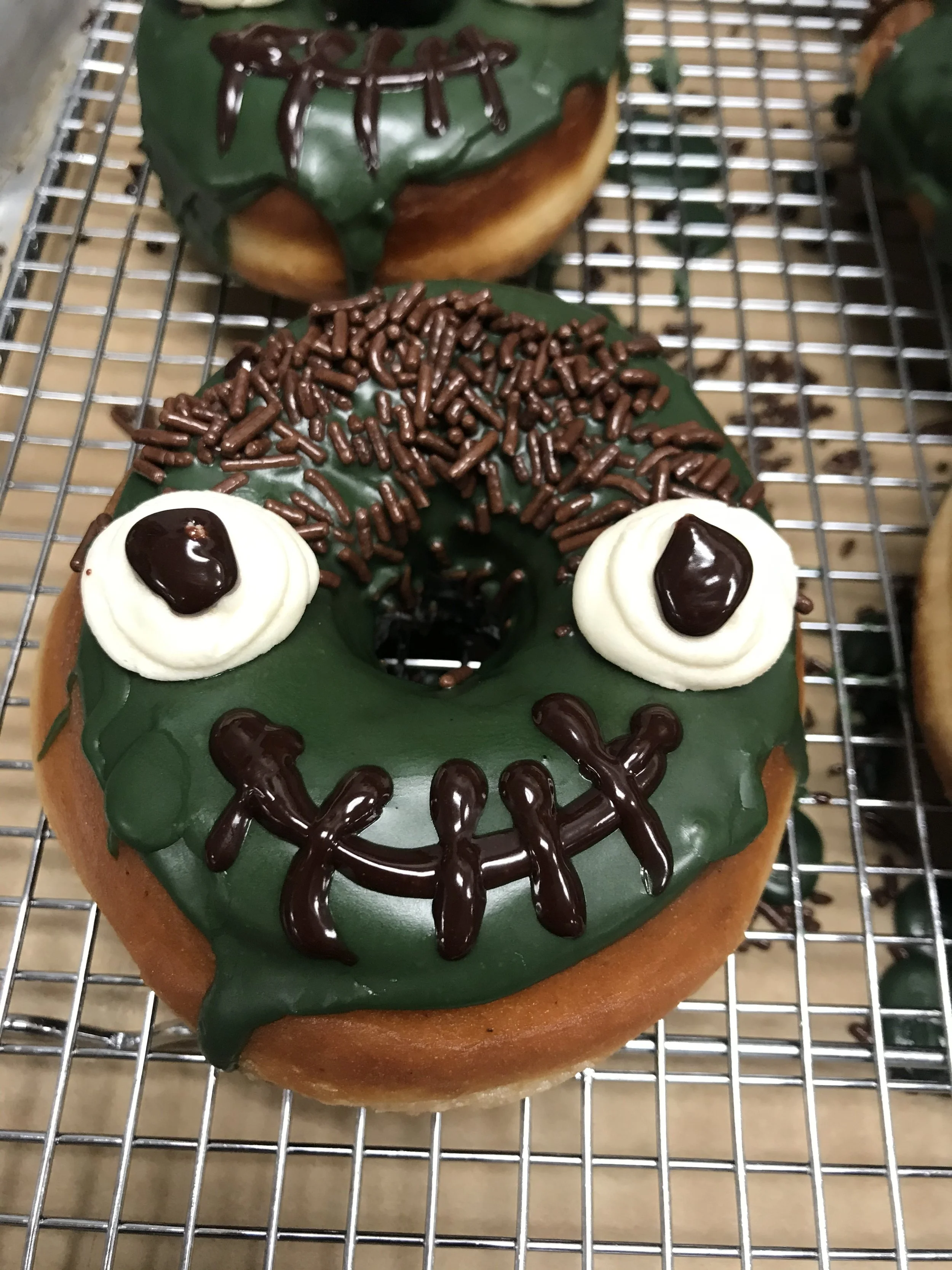 Frankenstein Doughnuts with colored glaze, vanilla frosting, chocolate ganache, & chocolate sprinkles