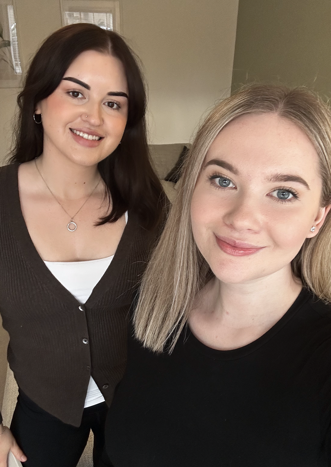 Two women taking a selfie indoors, smiling at the camera.