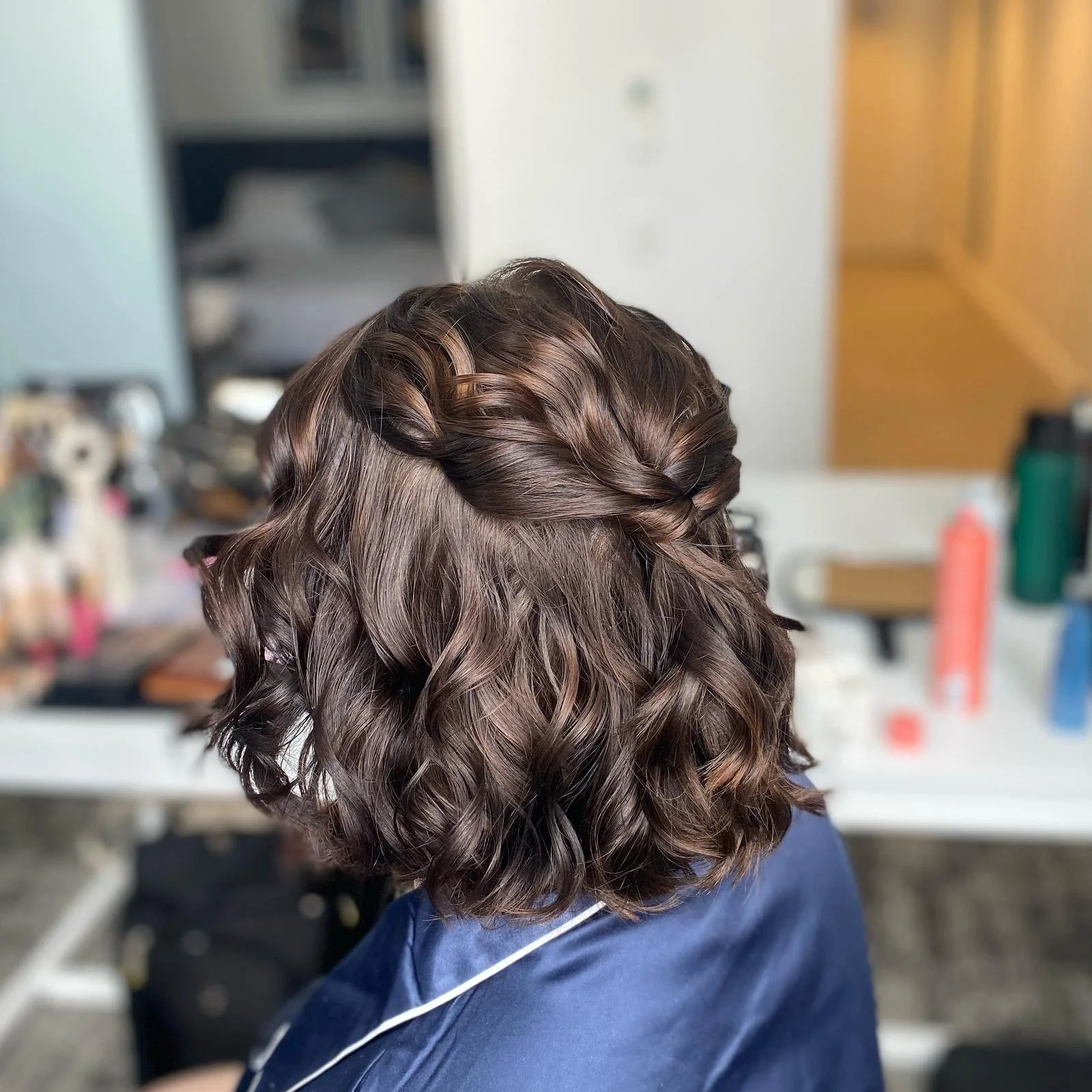 Back of a person's head with shoulder-length, wavy brown hair styled with a twisted braid on top.
