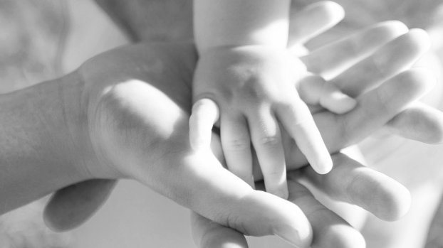 Close-up of a baby’s hand resting in an adult’s hand, showing connection, care, and early relationship