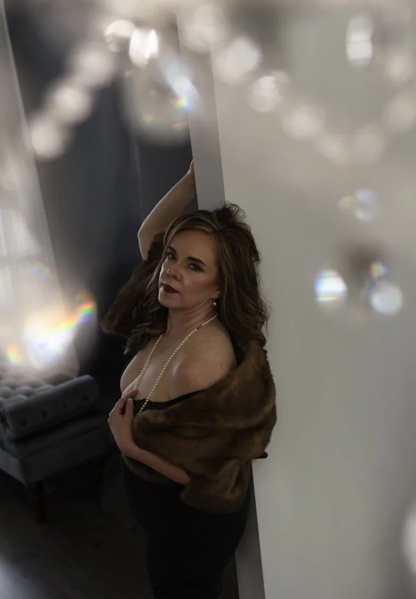 beautiful woman over forty leaning with one hand on the wall and the other brushing her chest with a pearl necklace
