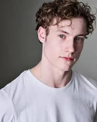 Ben Oatley who plans Aaron Samuels in Mean Girls which arrives at the Wales Millennium Centre in Cardiff is seen here in a white t-shirt looking at a side angle into the camera lens as part of a series of promotional headshot images