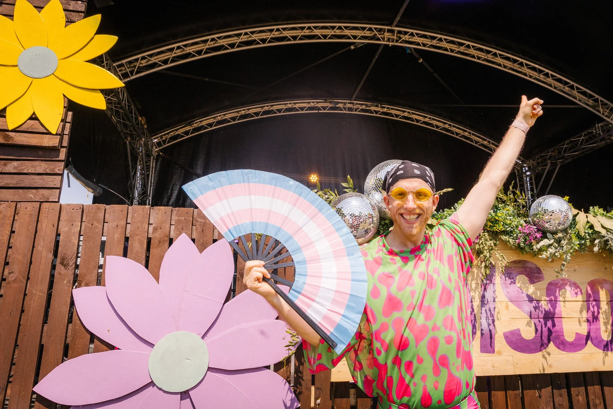 Festival guest with colourful fan, clothing and disco balls in front of the stage