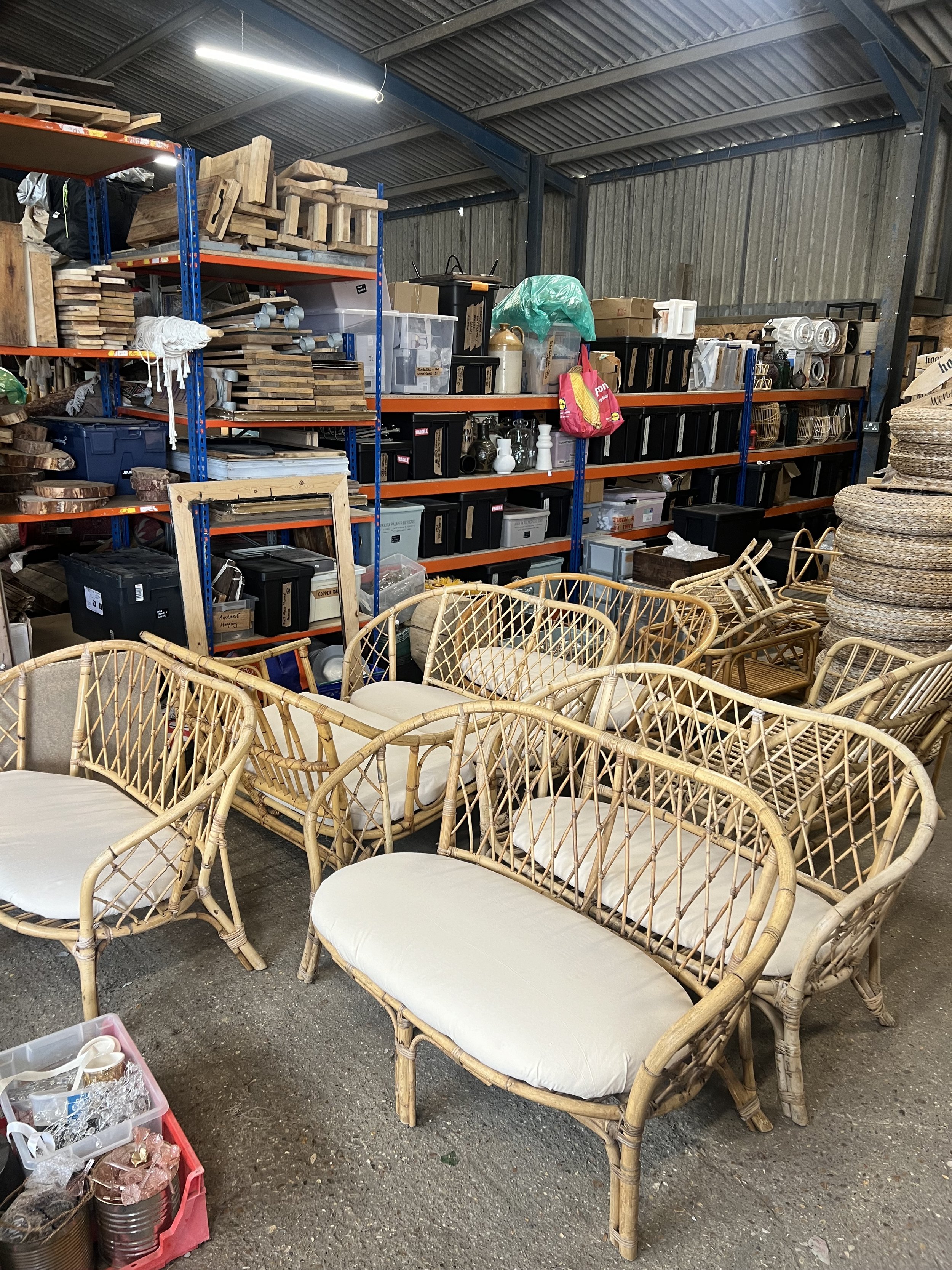  Vintage rattan and cane sofas with white linen seating lined up in a prop warehouse. Available for weddings, festival hire and events. 