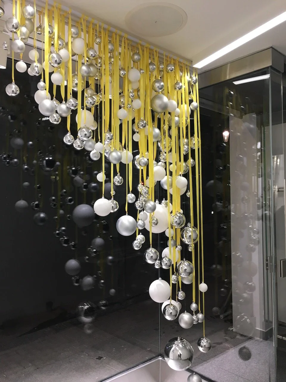 Cluster of silver baubles hanging from the ceiling with yellow ribbons, festive installation at SoulCycle London.