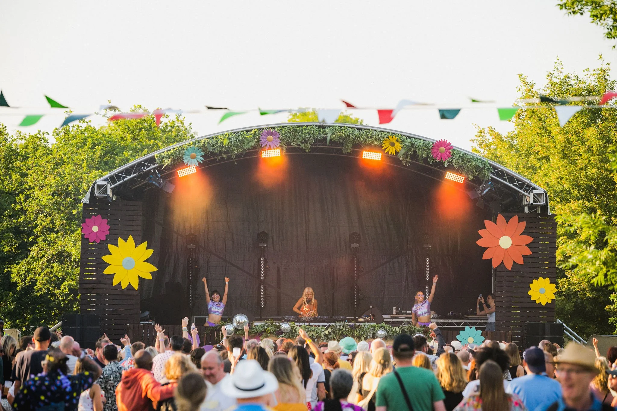 A festival stage with floral decor and dancing crowd.