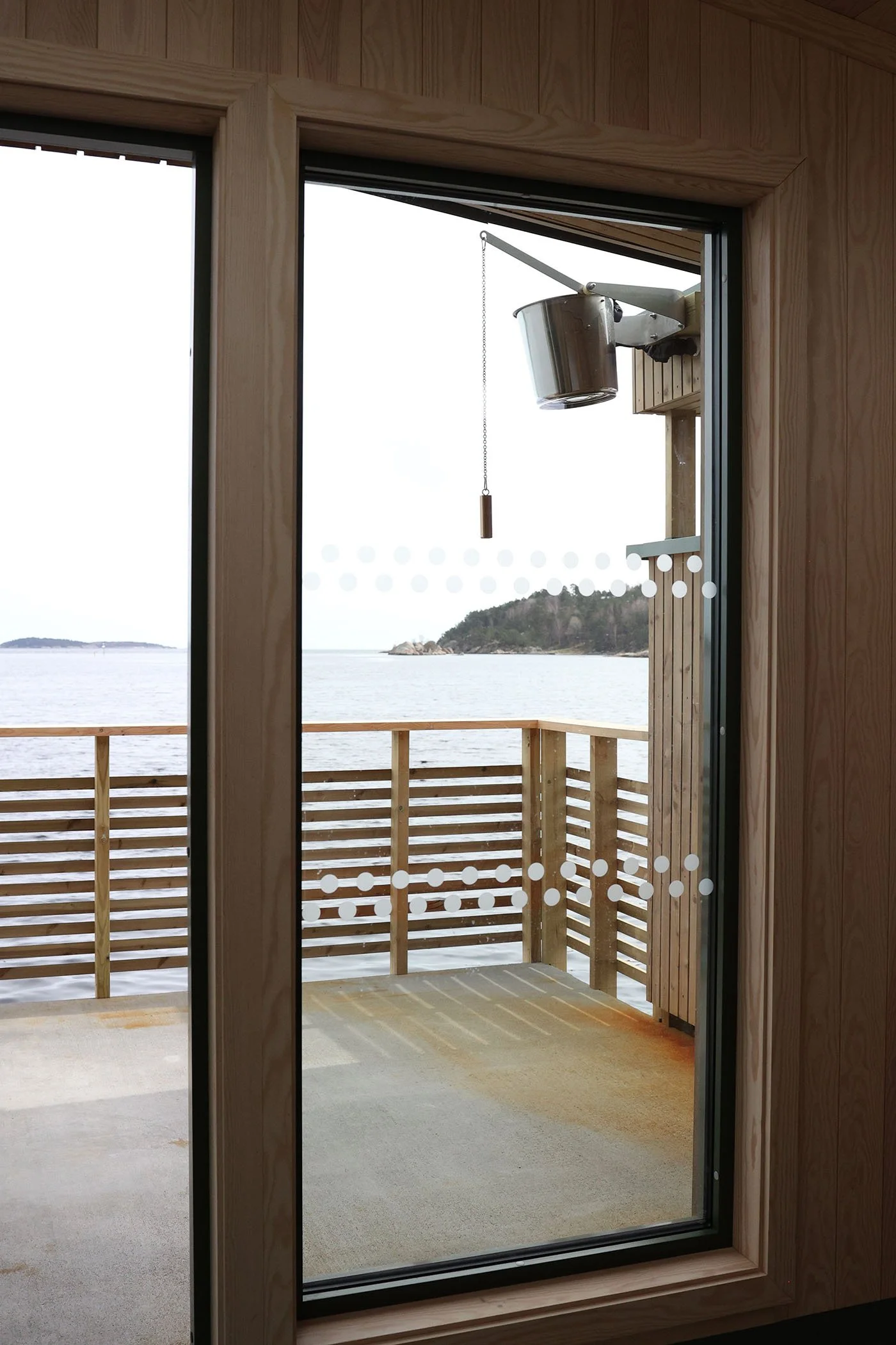 Utsikt fra en badstugarderobe ut en glassdør til en balkong med havet i bakgrunnen.