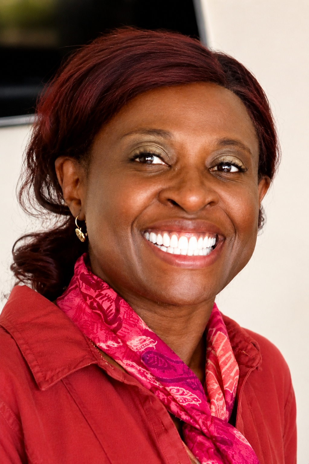 Dr. Bola Sogade, founder and medical director of ObGyne Consultants, smiling in a red jacket and patterned scarf.