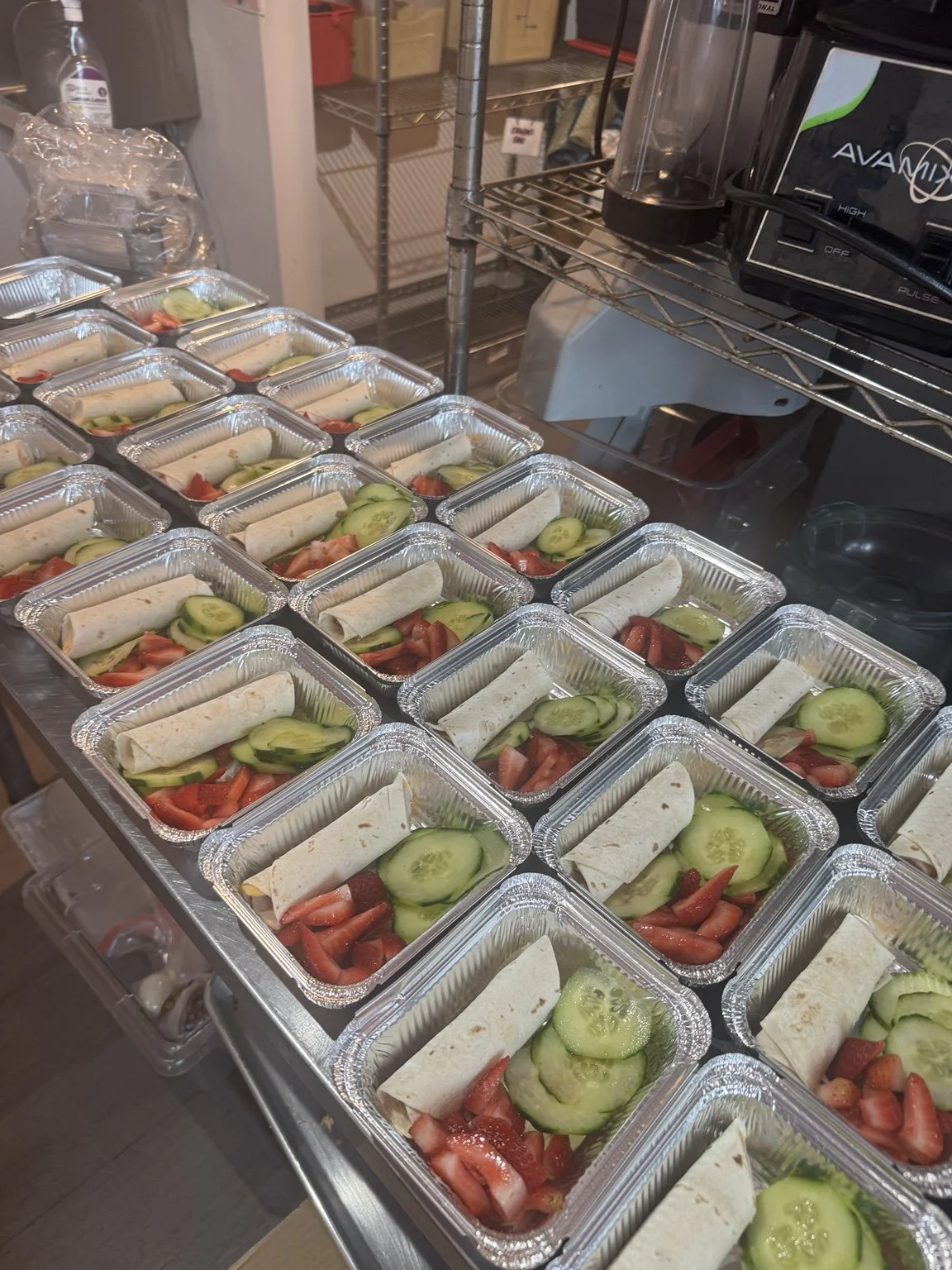 Rows of individually prepared wrap meals with cucumber and strawberries.