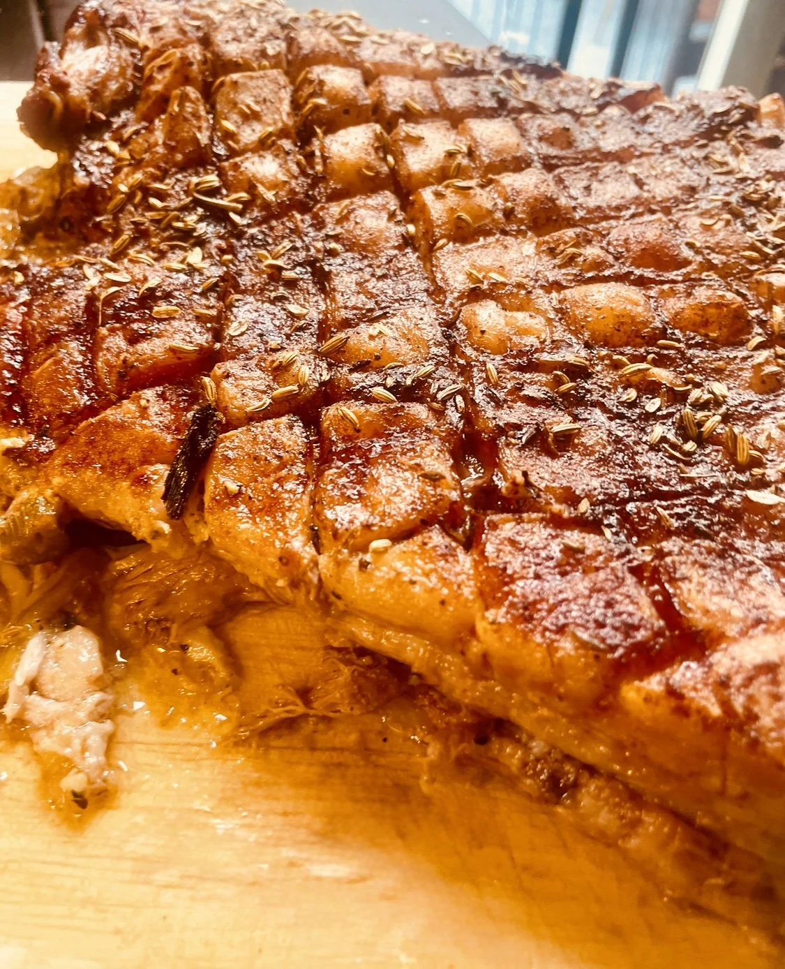 Roasted pork belly with a golden-brown scored crust on a wooden cutting board.