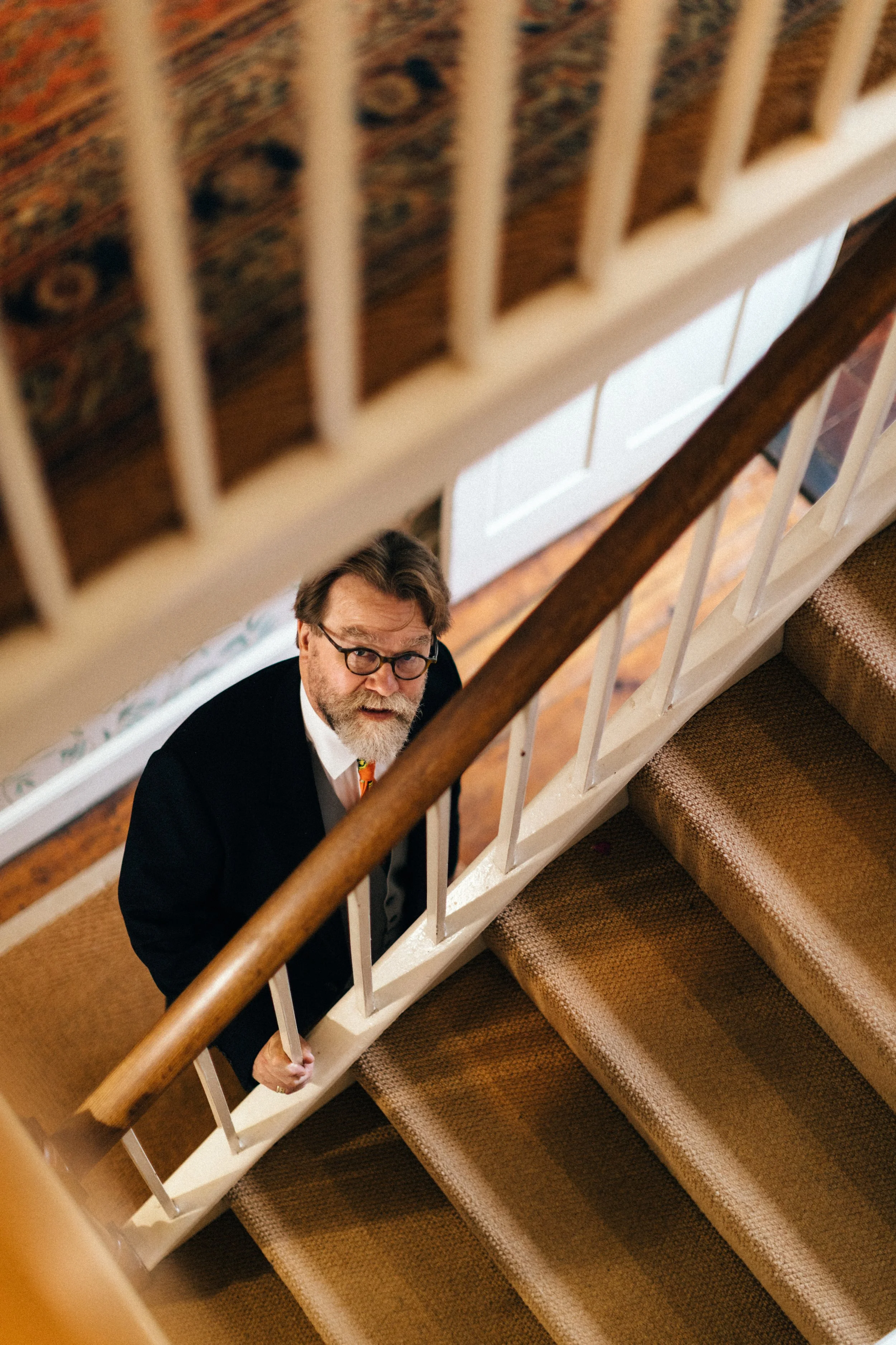 Father of the bride with glasses and a beard looking up from the bottom of a staircase.
