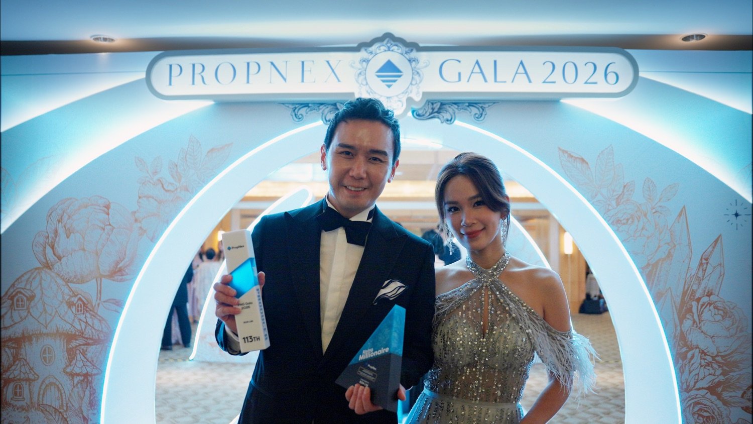 Ron Lim and Ming Hui at Propnex Top performing realtors gala event. Ron is holding a trophy for one of the top performing real estate agents in Singapore. The event backdrop reads 'PROPENEX GALA 2026'.