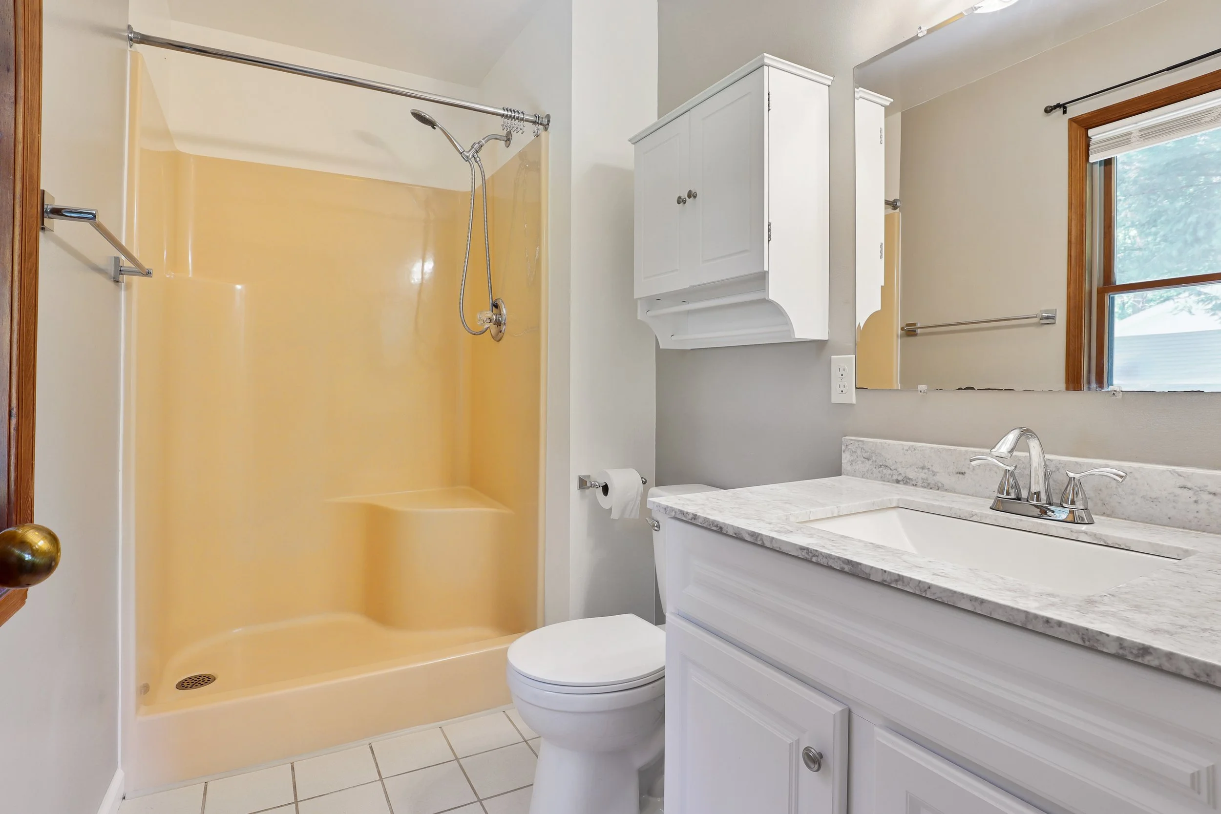 Bathroom with a yellow shower, a white toilet, a marble countertop sink, a mirror, and a window.