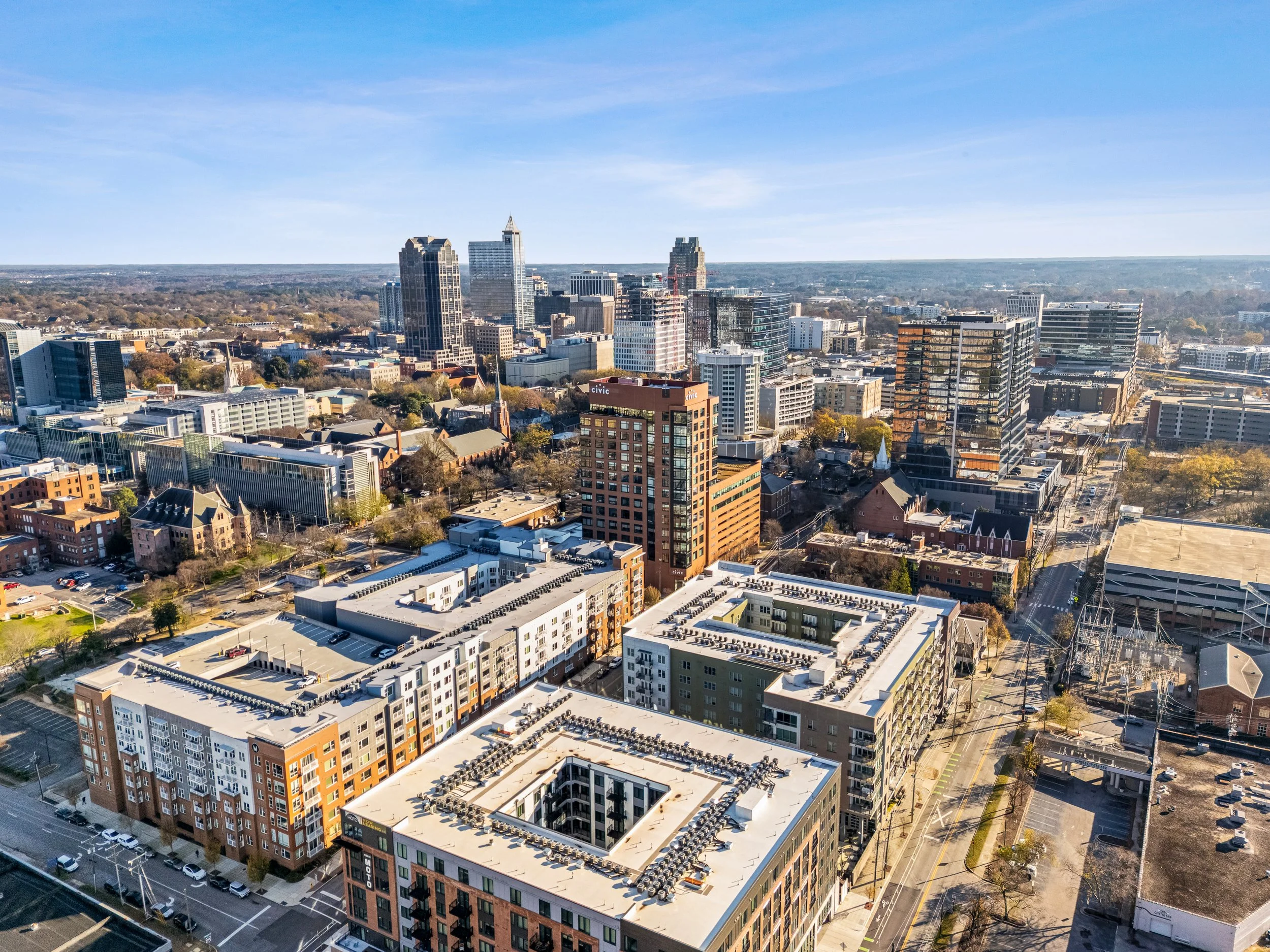 Aerial view of a suburban neighborhood with houses, a curved street, a nearby lake, and lots of green trees.
