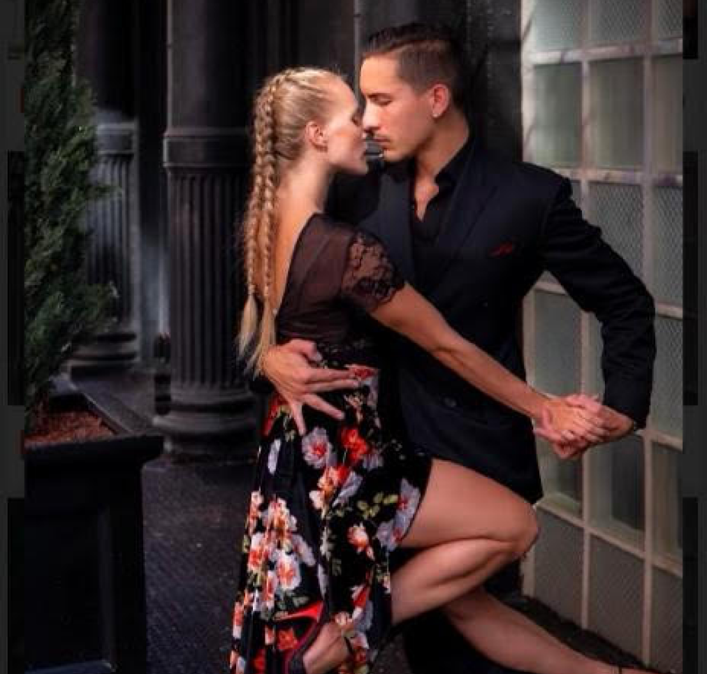 A couple dancing passionately in a close embrace, with the woman wearing a floral dress and the man in a black suit.