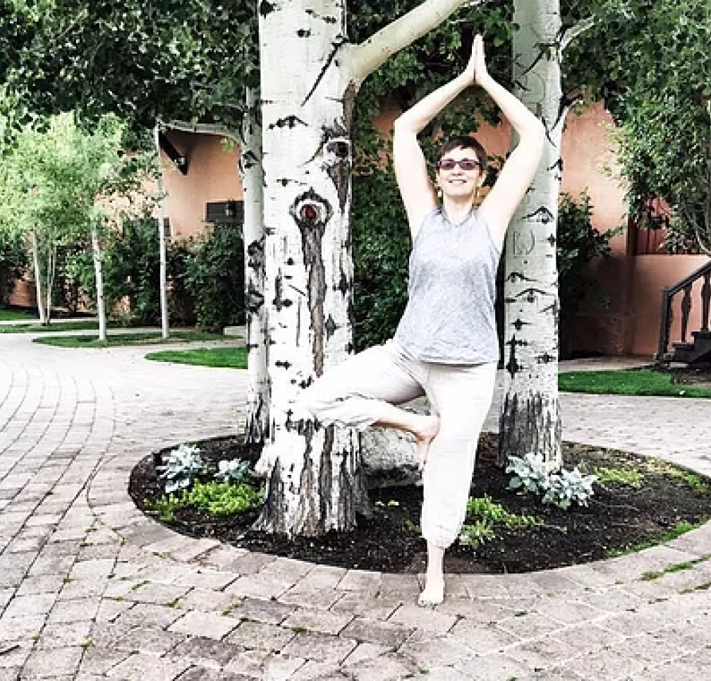 Person practicing yoga in tree pose outdoors near a birch tree.