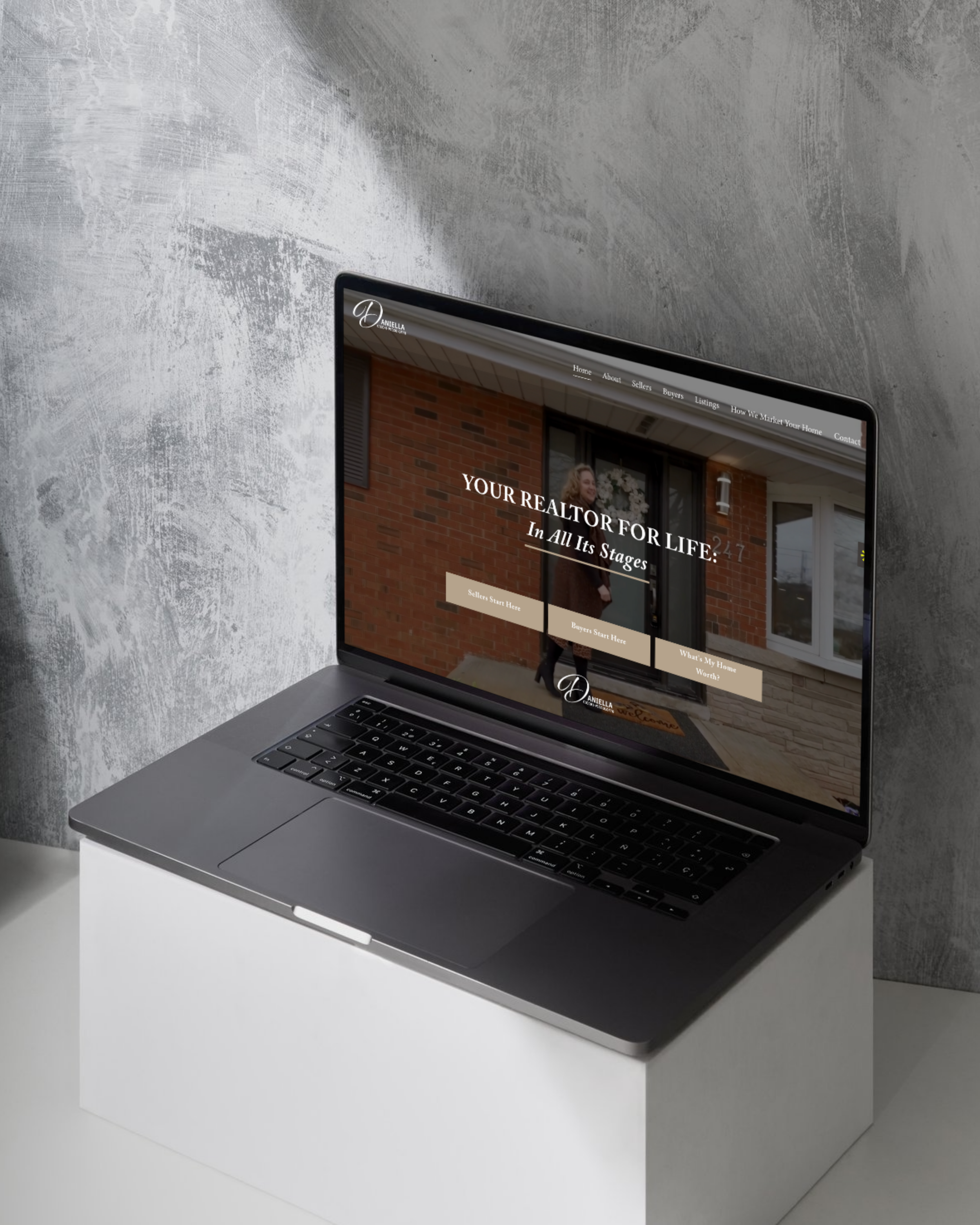 Laptop on a white block displaying a real estate website with a woman standing in front of a house.