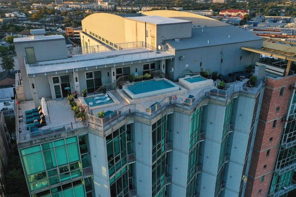 A rooftop terrace with a small pool, hot tub, seating area, and potted plants on a high-rise building in an urban area.