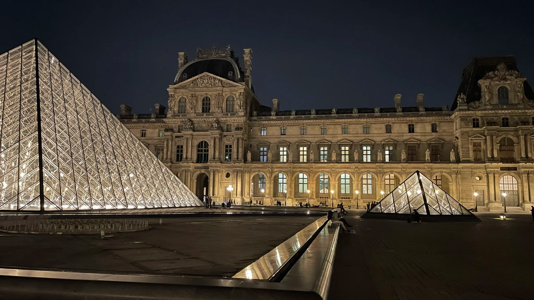 Night view of the Louvre Museum in Paris, France, showing illuminated glass pyramids in front of the historic building.