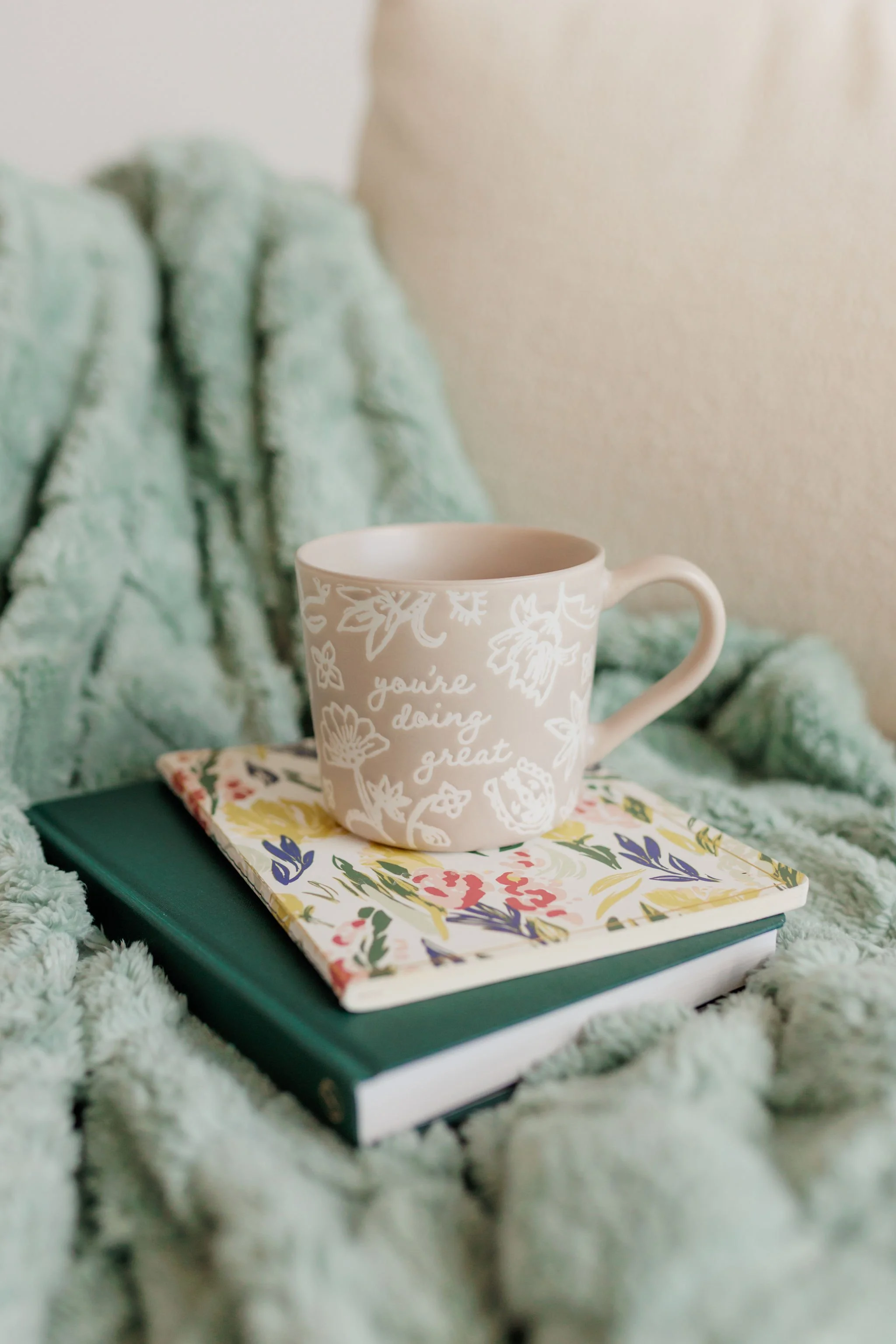 Ceramic mug on stacked notebooks resting on a soft green blanket