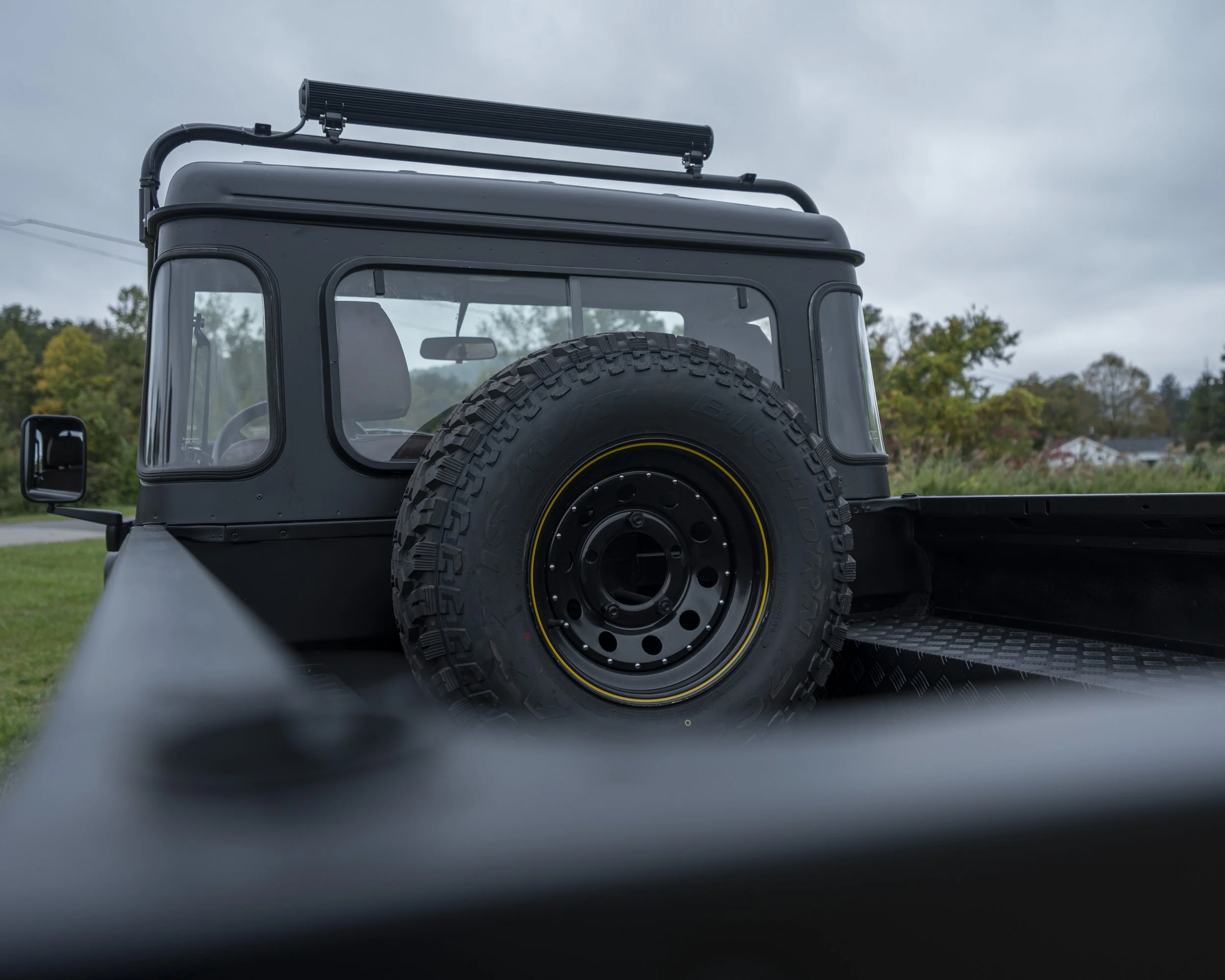 A black off-road vehicle with a spare tire mounted on the back, parked outdoors on a cloudy day.