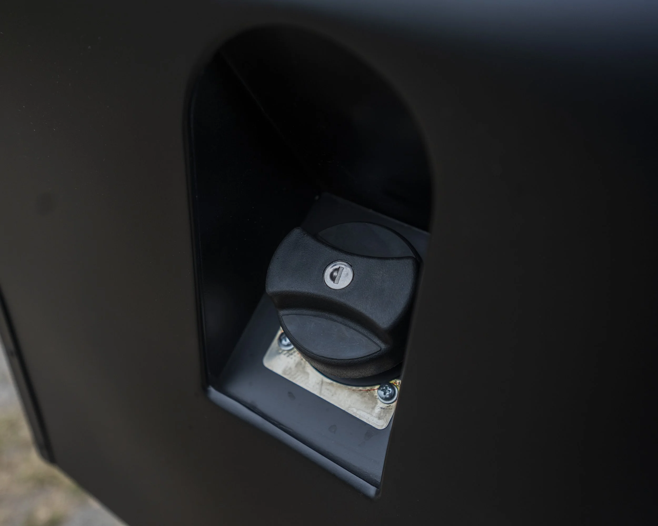 Close-up of a black electric vehicle charging port with a covered socket on a dark vehicle exterior.