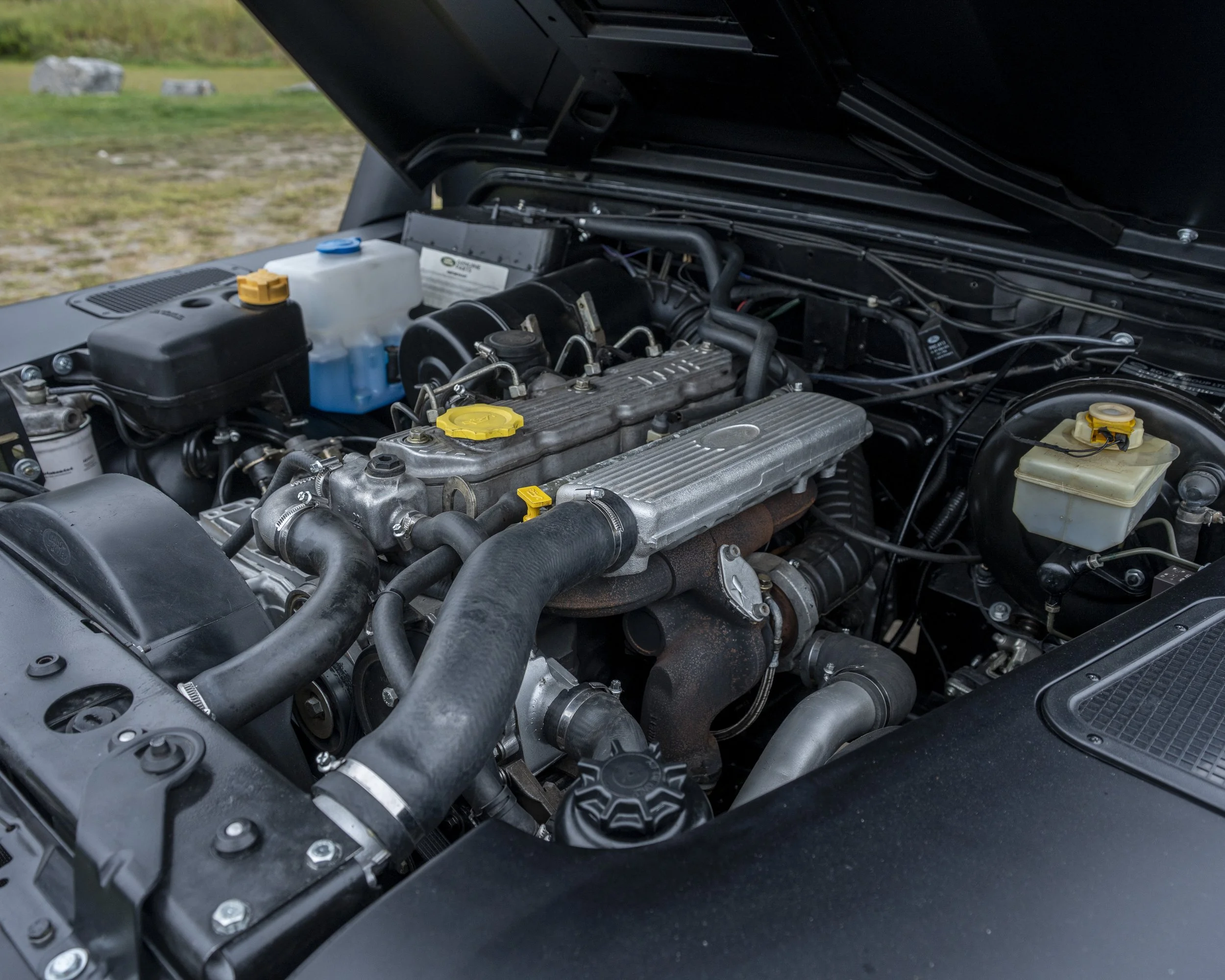 Close-up of a car engine bay with various components, hoses, and fluid reservoirs.