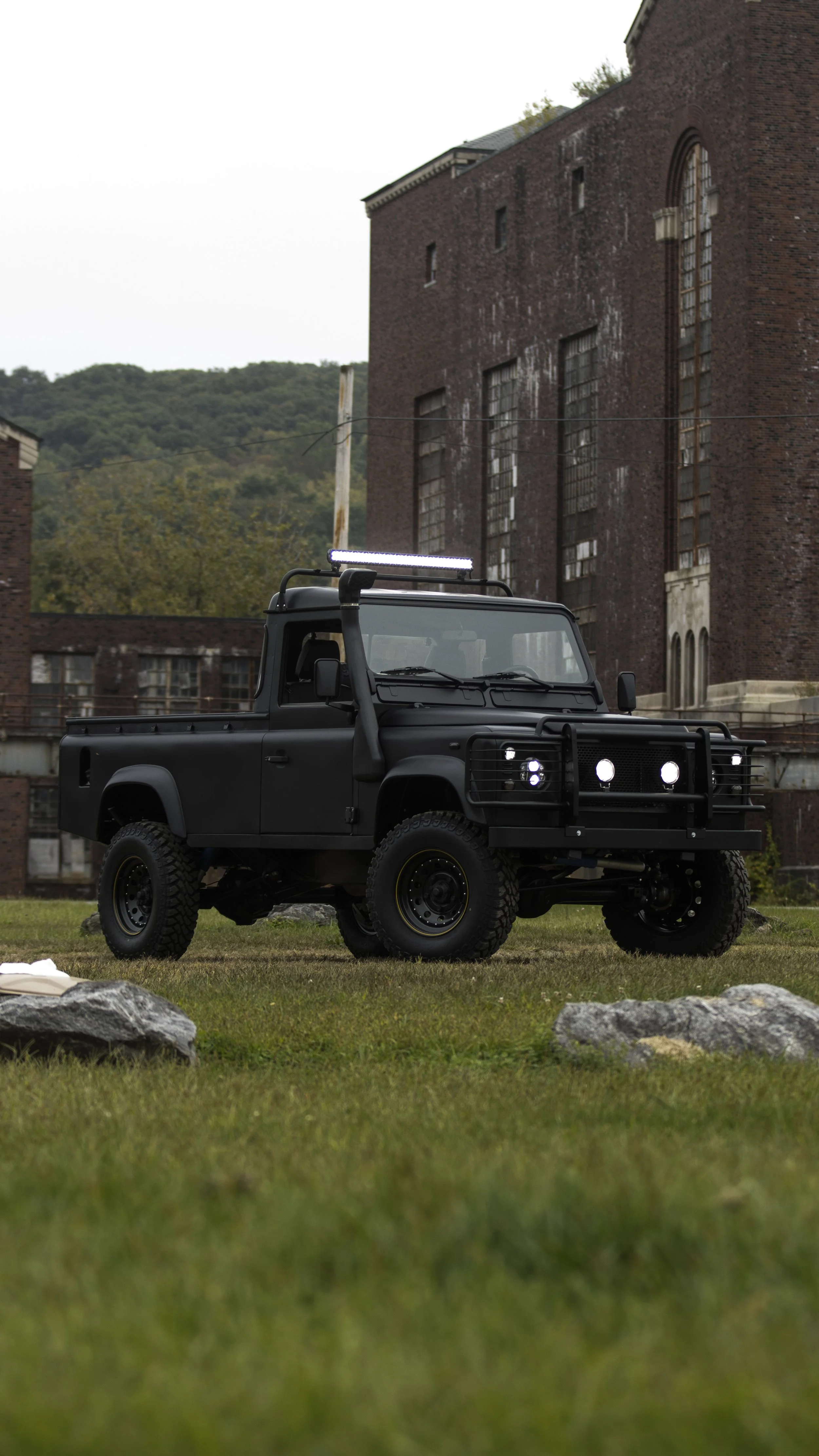 A black off-road vehicle parked on grass in front of an old brick building with large windows.