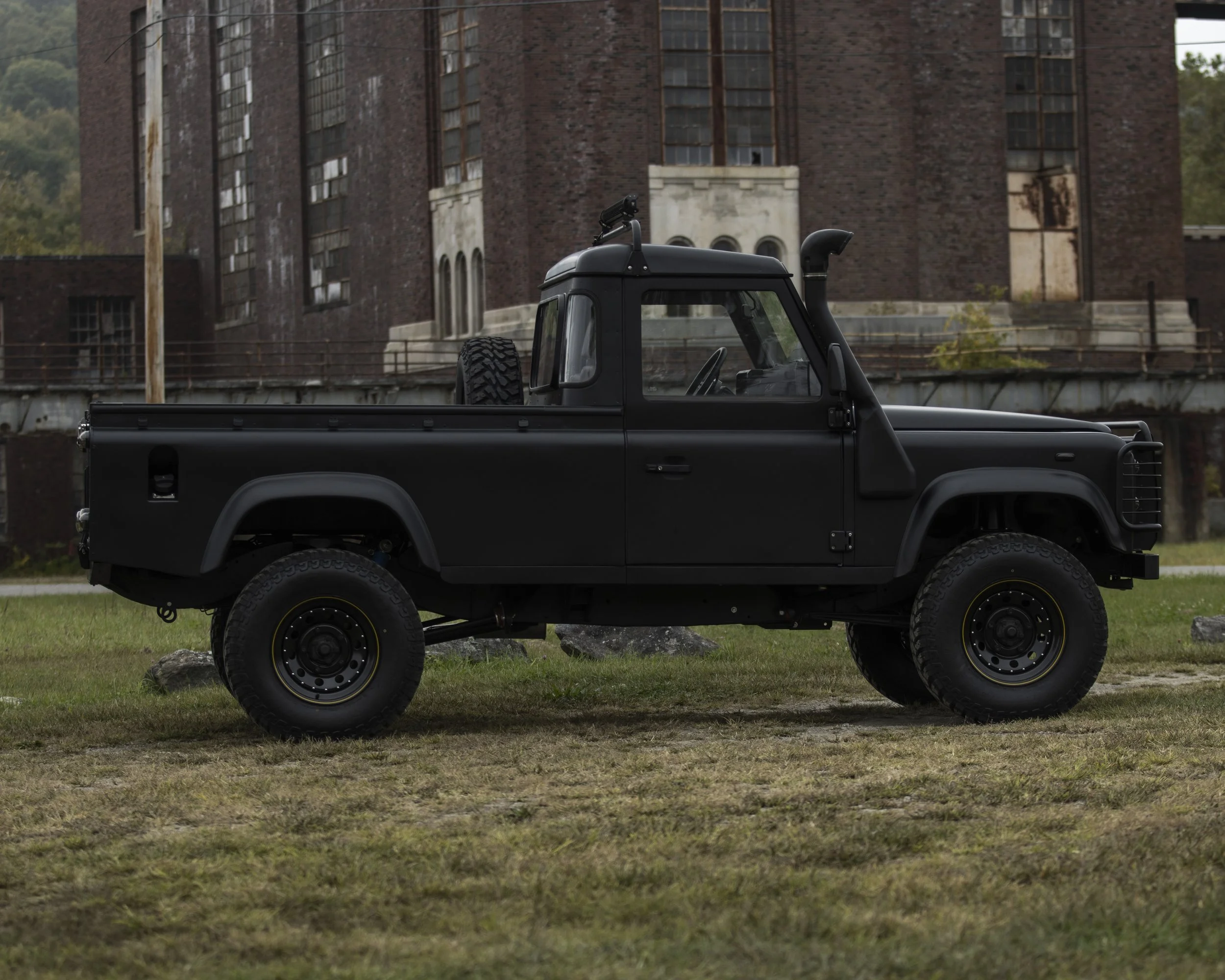 A black off-road pickup truck parked on grass in front of an old brick building.