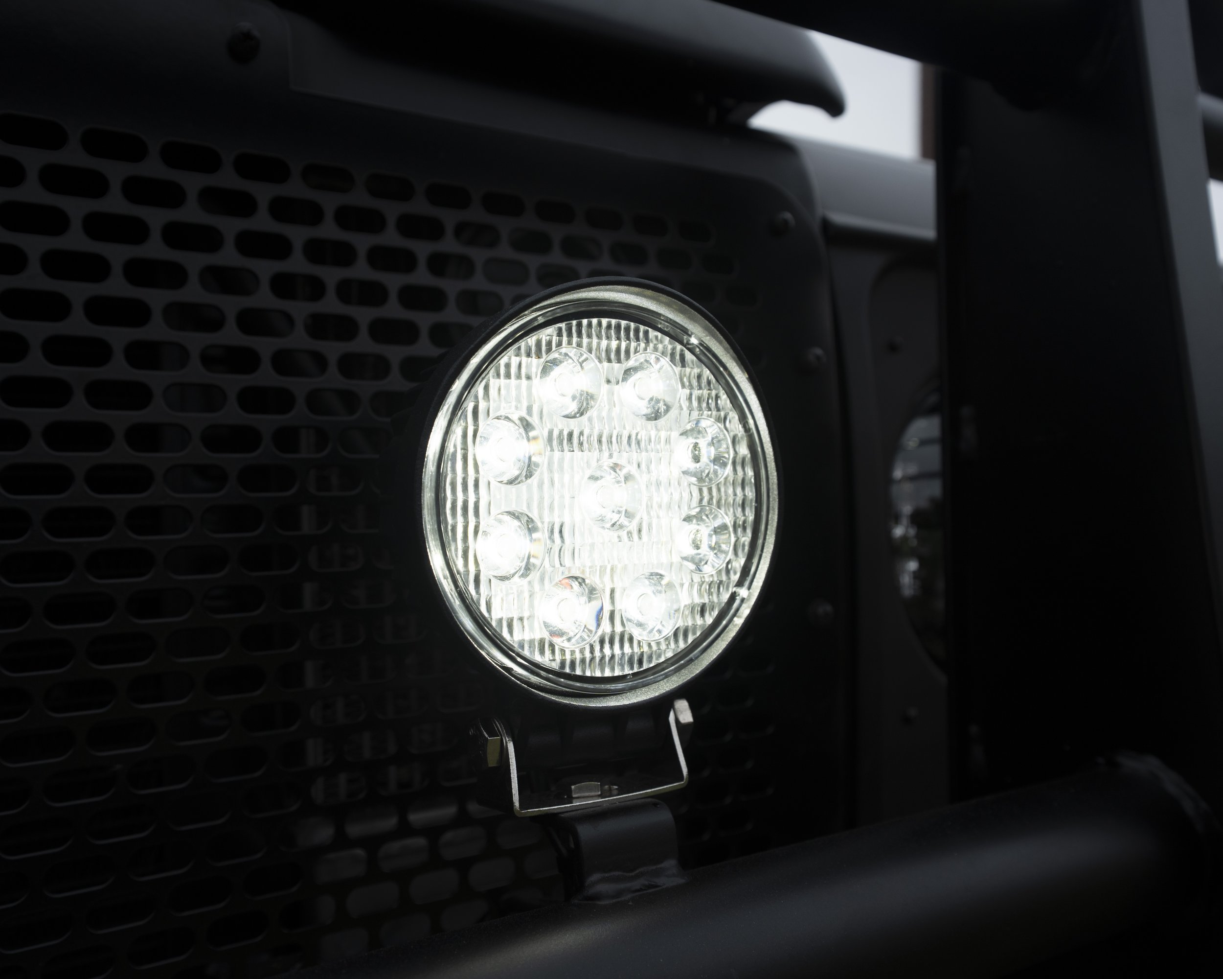 Close-up of a bright LED light mounted on the front of a vehicle, with a black grille in the background.