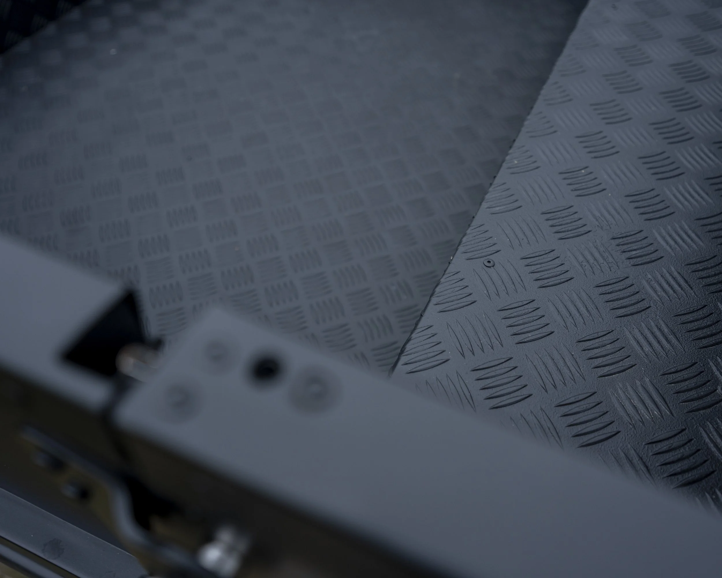 Close-up of a metal platform with a diamond plate pattern, showing part of a black electronic device with input ports.