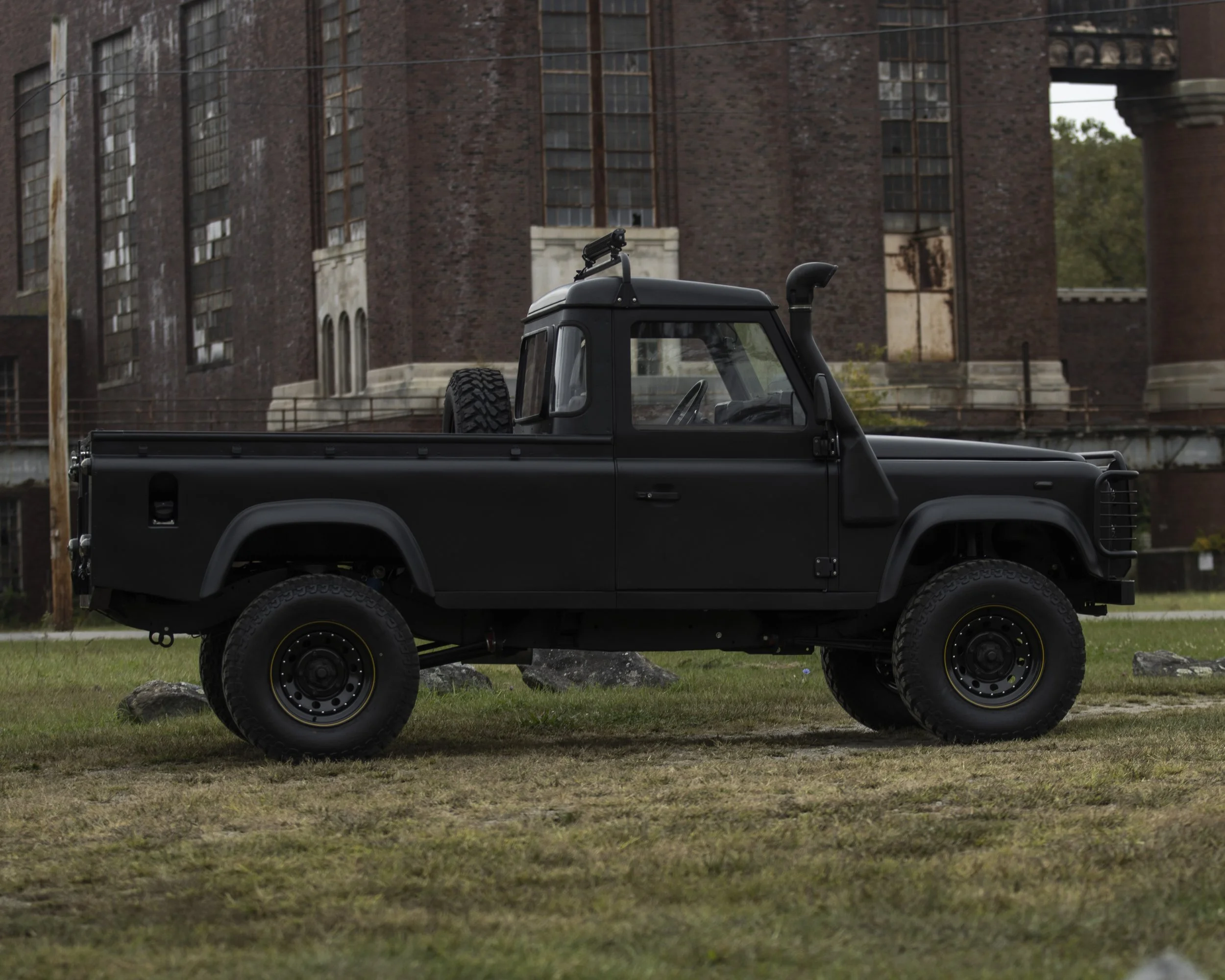 A black off-road truck parked on grassy ground with an old brick building in the background.