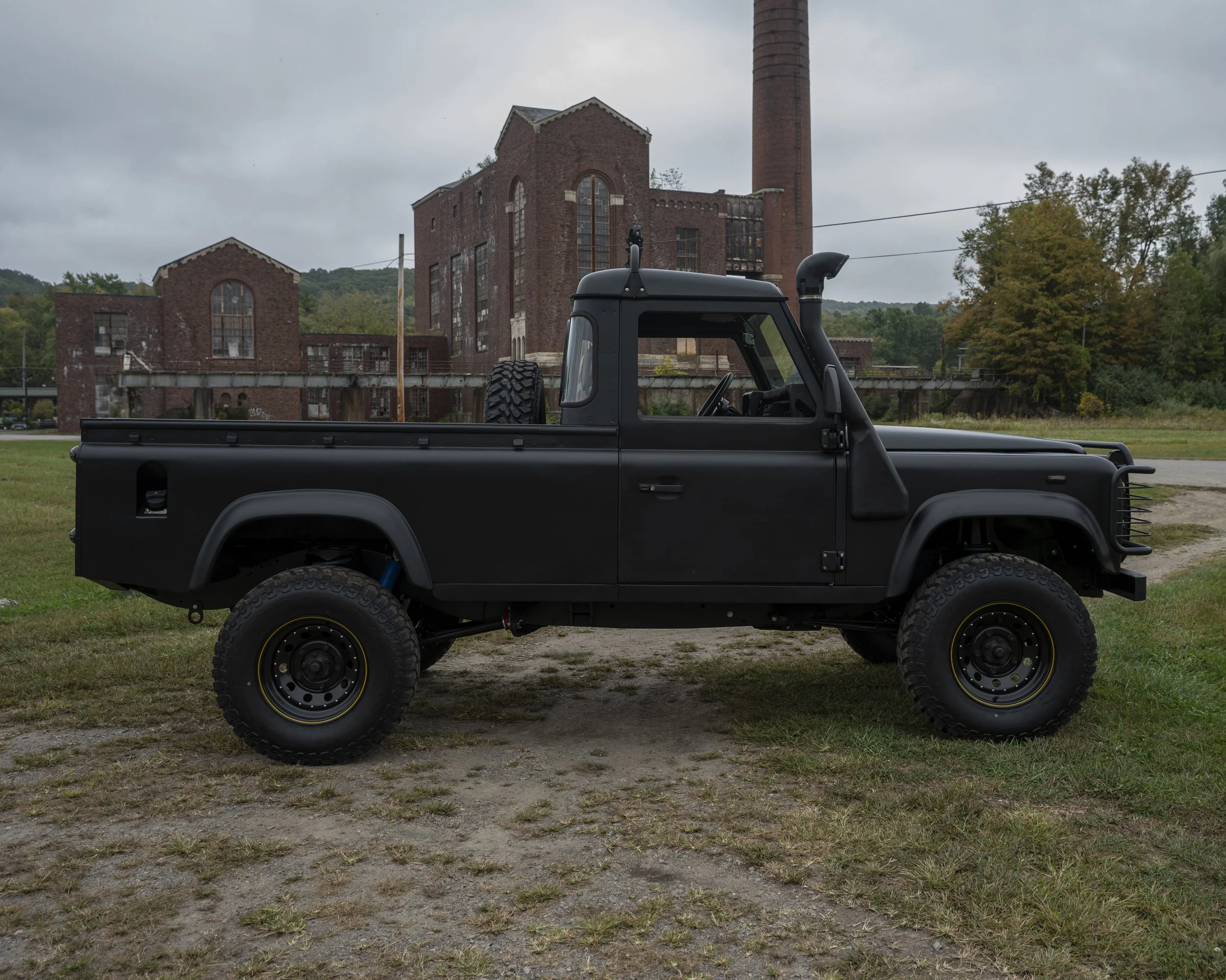 A black pickup truck parked on grass with an industrial building and trees in the background.