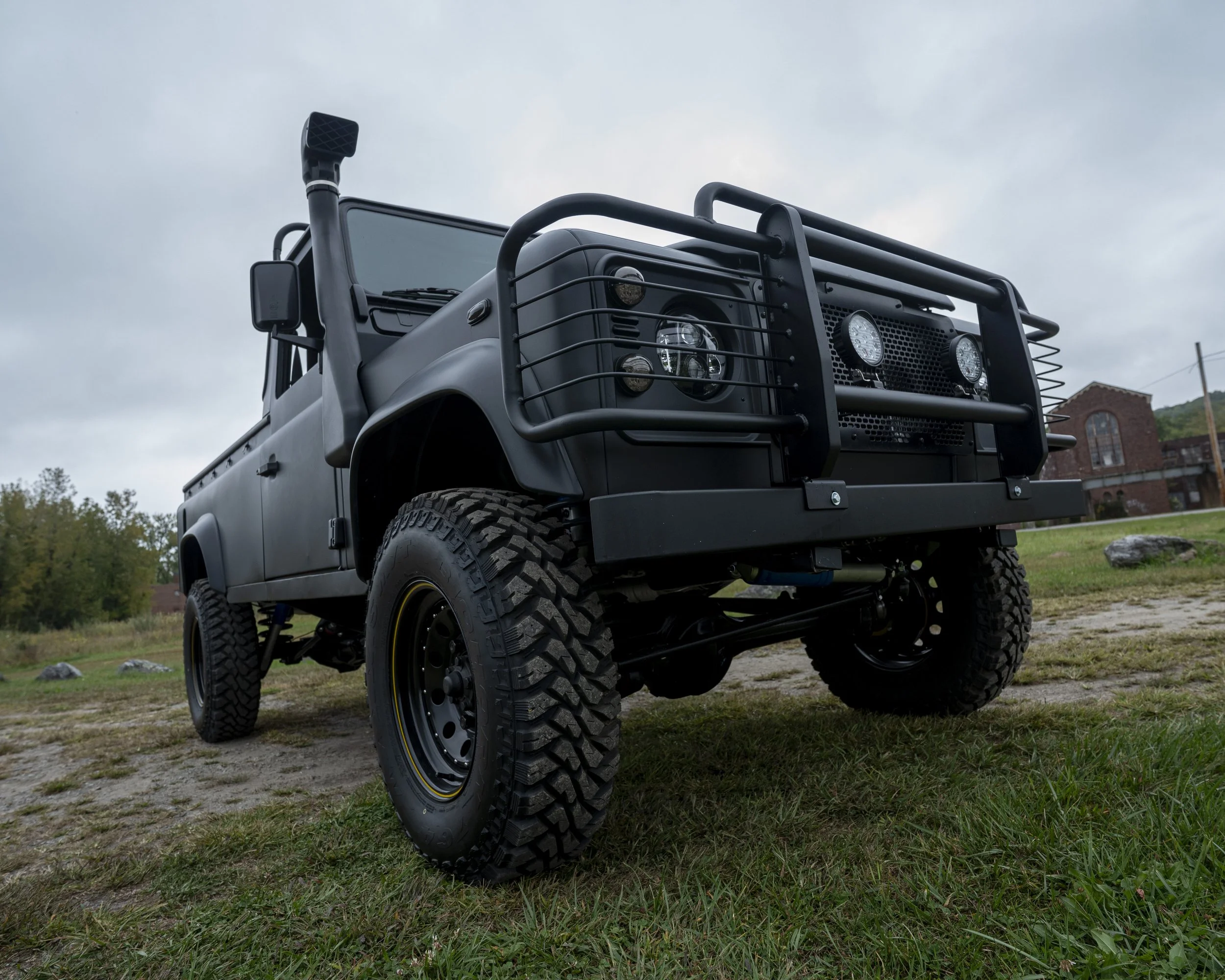 A black off-road utility vehicle with large tires and protective front grille, parked on grassy and dirt terrain under a cloudy sky.