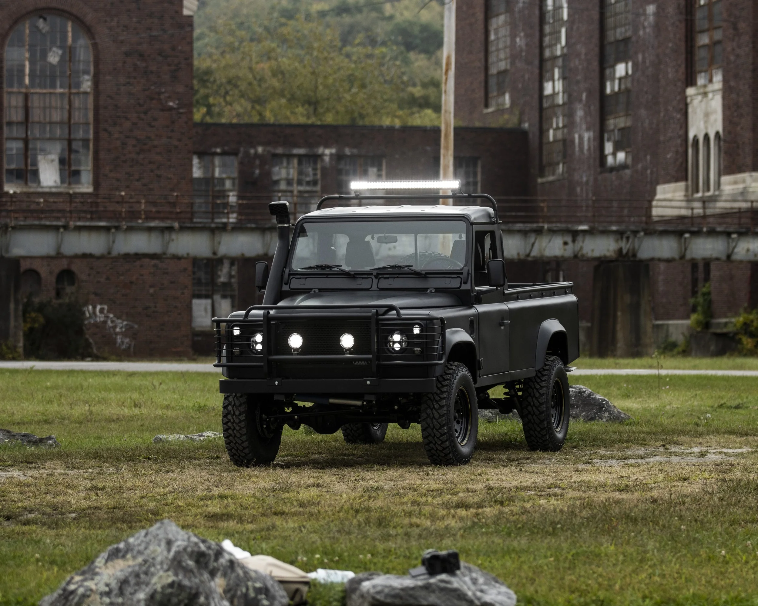 A black off-road utility vehicle with four large tires, parked on grassy terrain in front of old brick buildings.