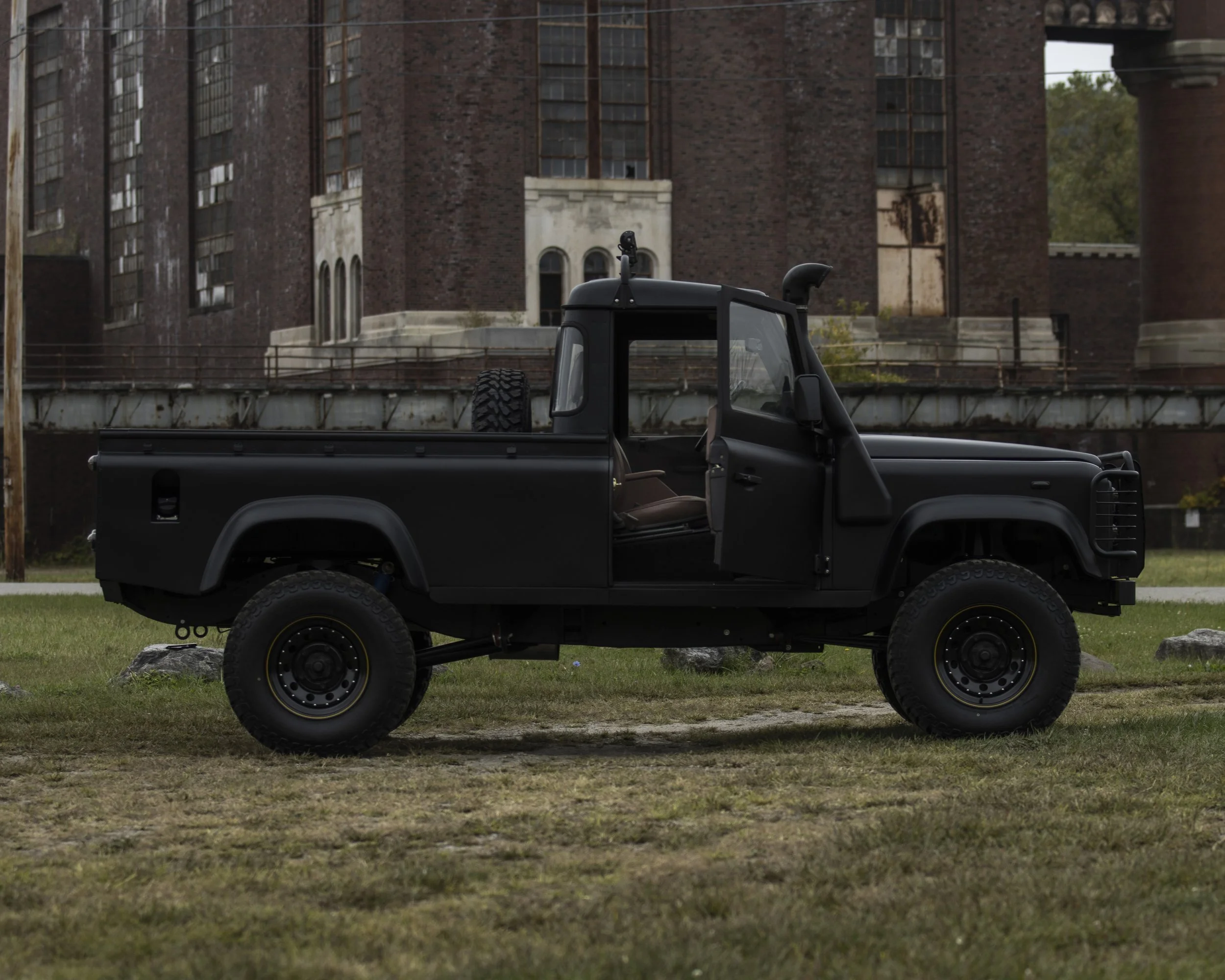 A black pickup truck parked on grass in front of a large, historic brick building with arched windows and multiple stories.