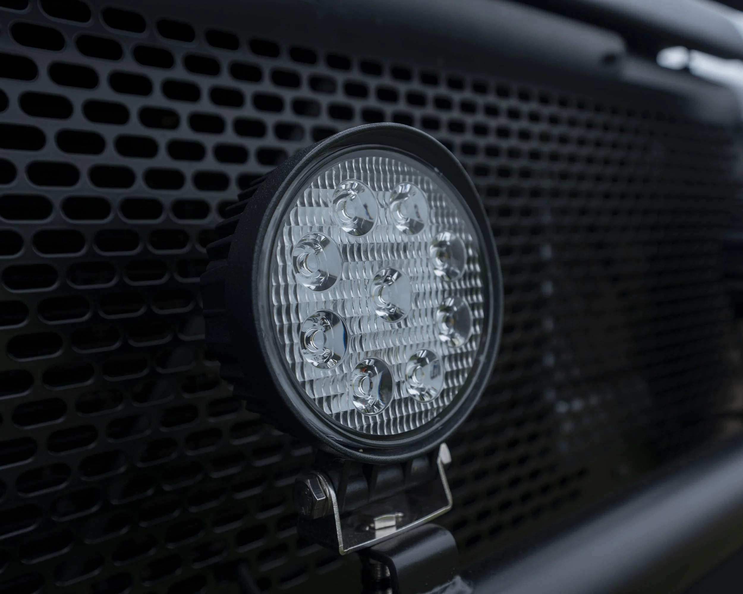 Close-up of a circular LED off-road light mounted on a vehicle's front grille with a black honeycomb pattern.