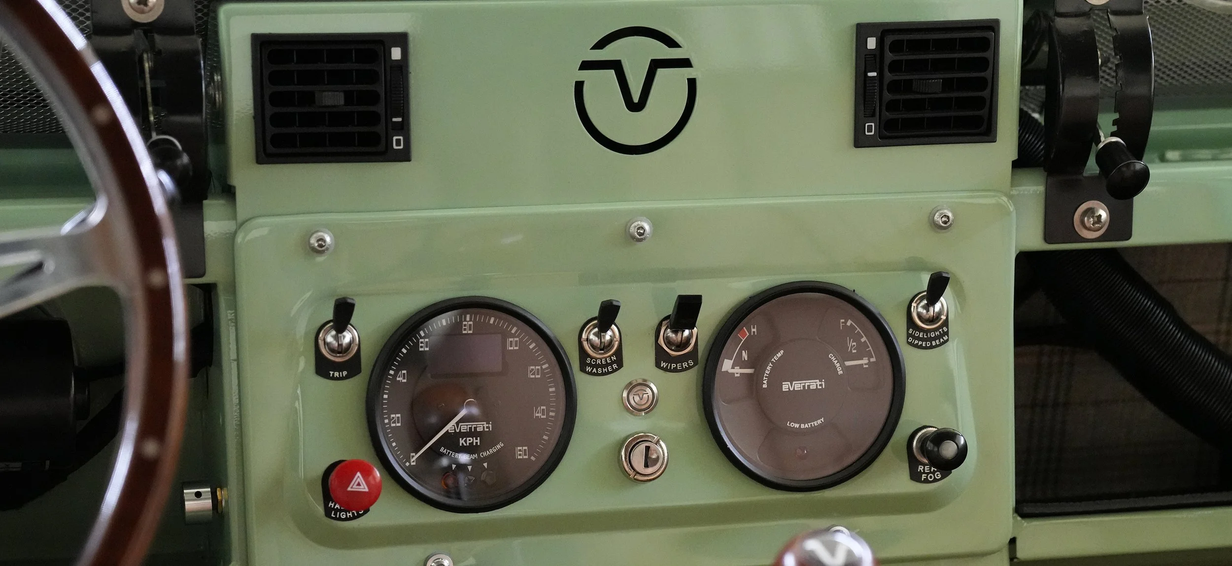 Close-up of a vintage vehicle dashboard with gauges, switches, and vents in a pale green color.