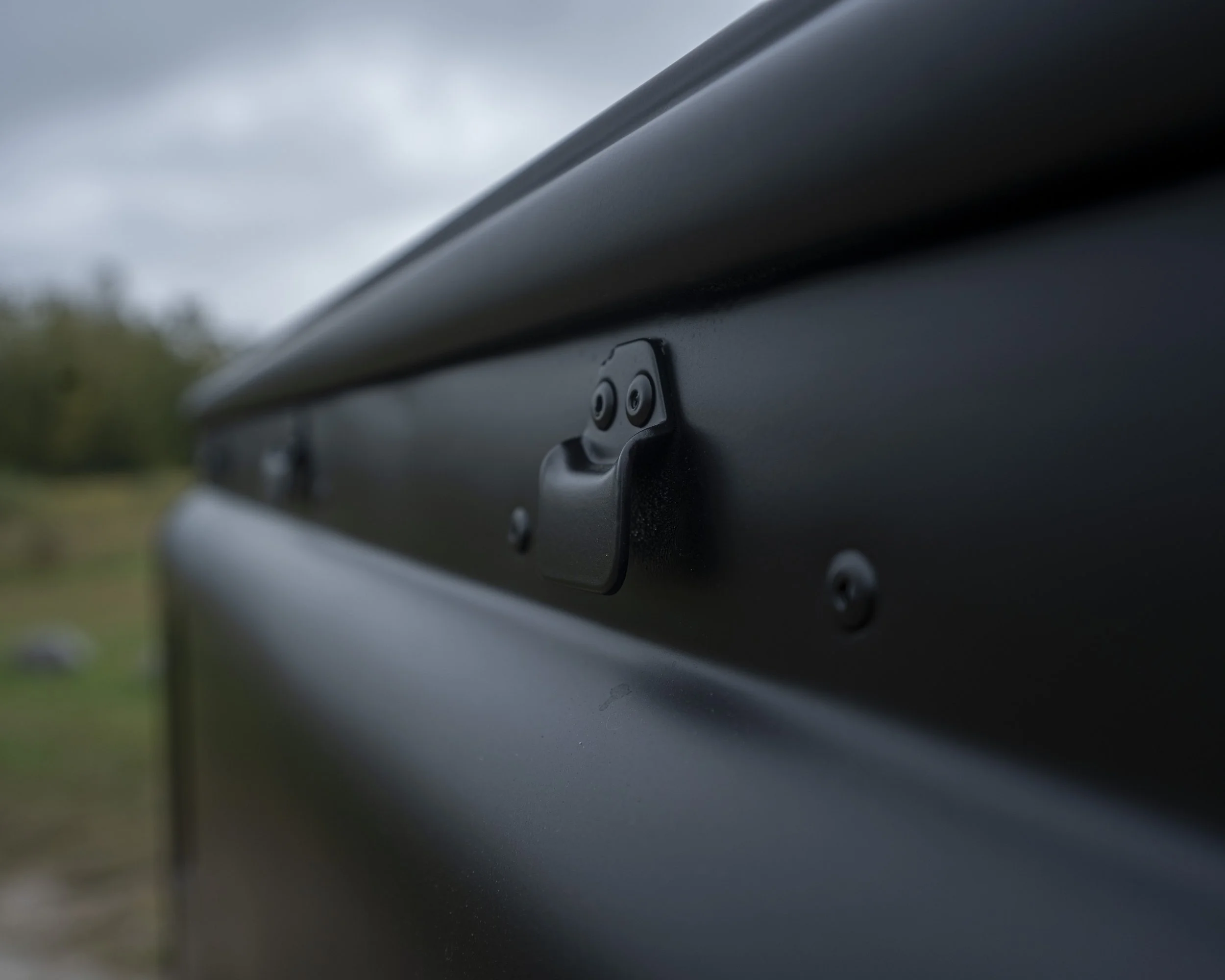 Close-up of a mailbox latch on a black mailbox with a blurred outdoor background.