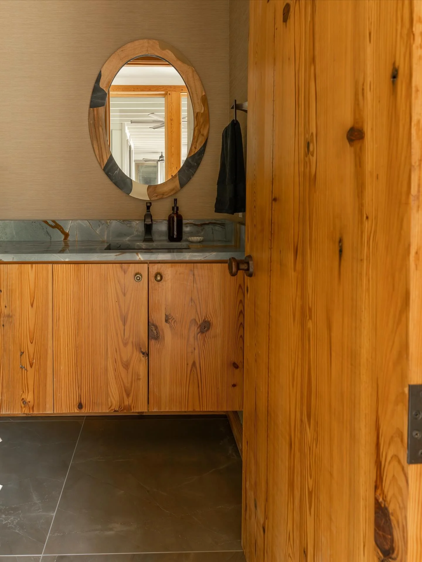 Knock knock. Swipe to see the before. We elevated this powder bath with new tile flooring, grasscloth wallcovering, a new mirror, and updated plumbing fixtures. The original pine cabinets and eclectic hardware add a touch of character.