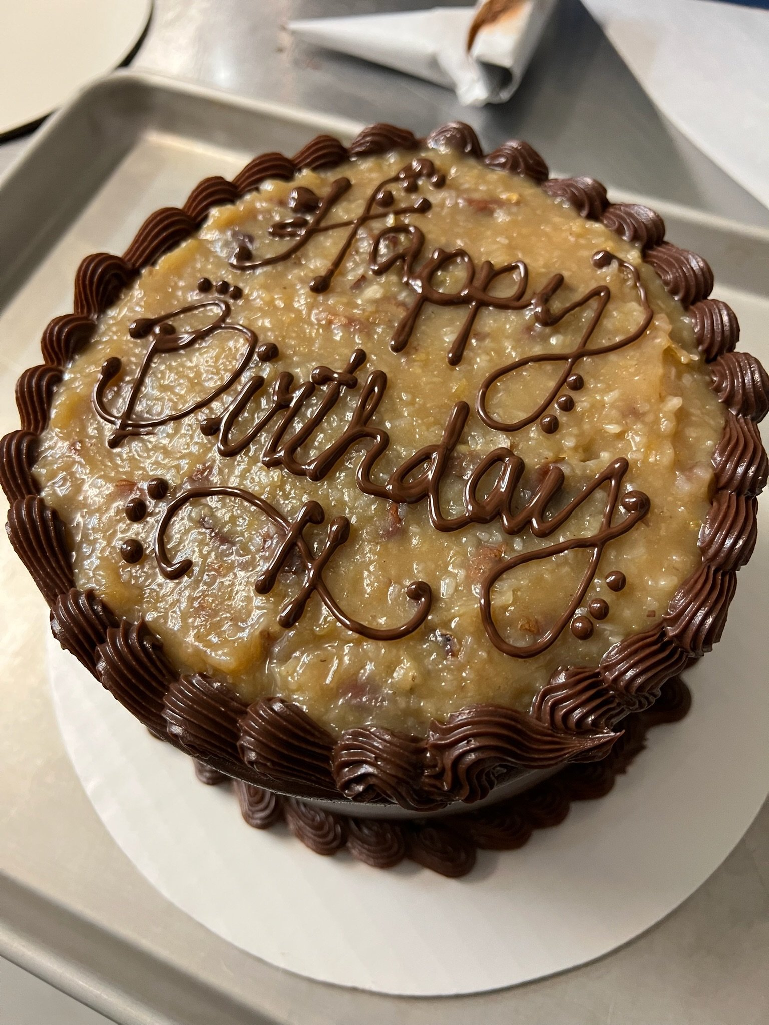 a german chocolate cake with chocolate frosting and a coconut topping that say happy birthday