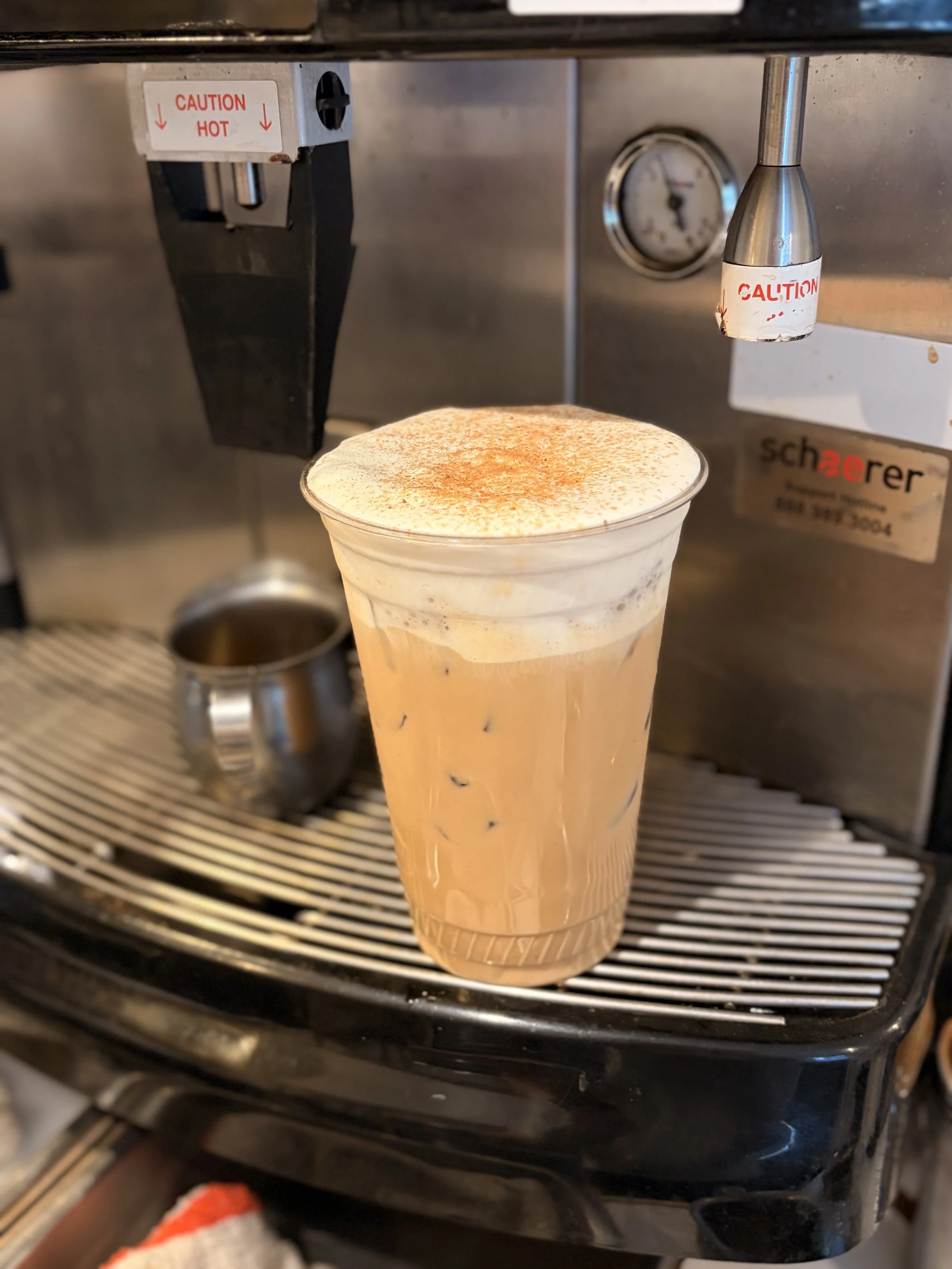 And iced coffee with a white cold foam sitting on an espresso machine