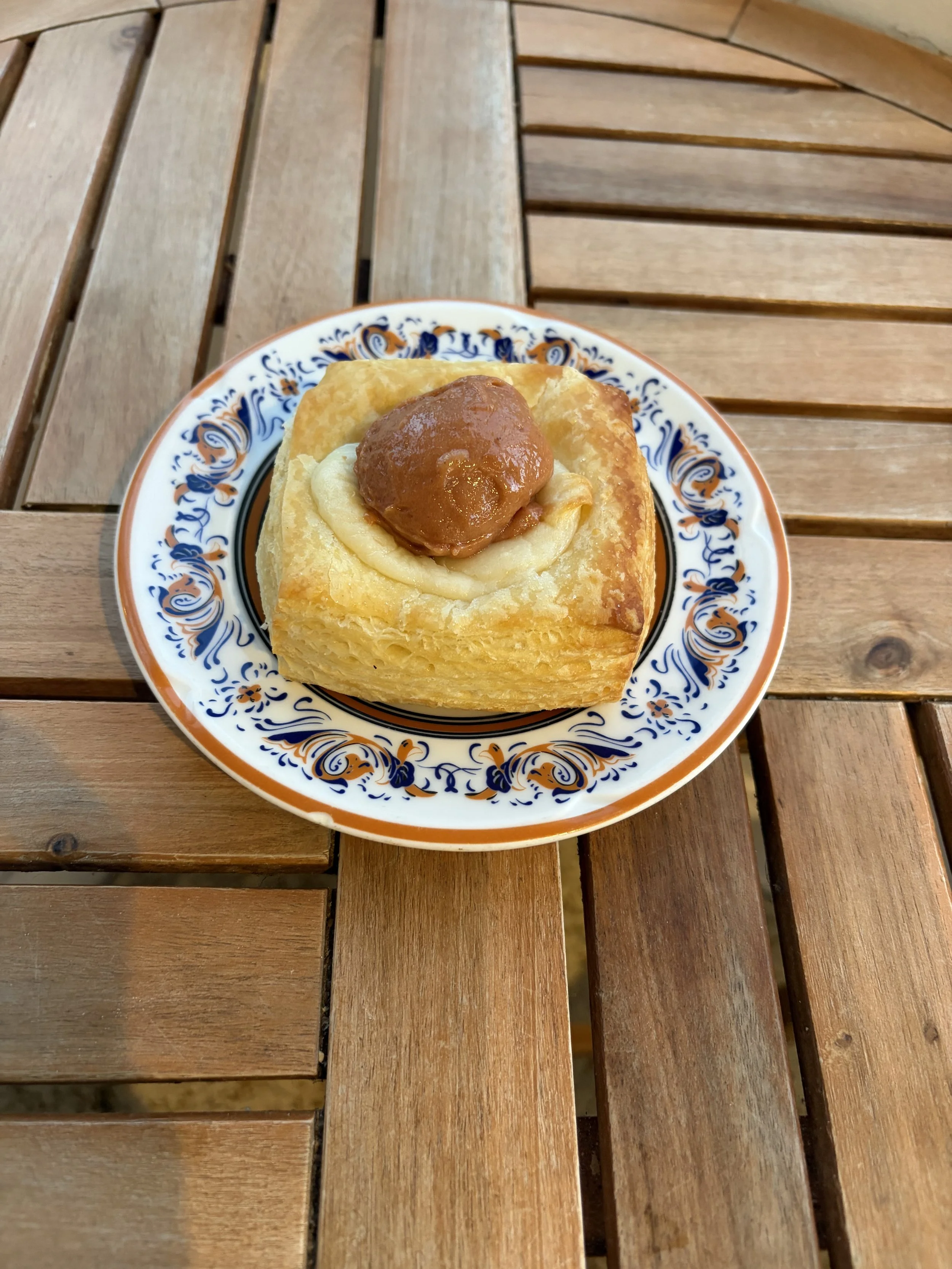 a guava danish bread on a china plate set on a wood table