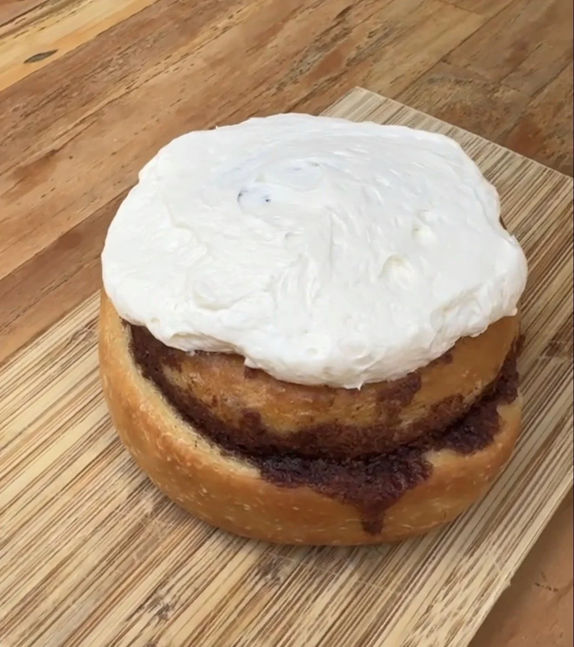 a cinnamon roll topped with white buttercream frosting on a wooden surface