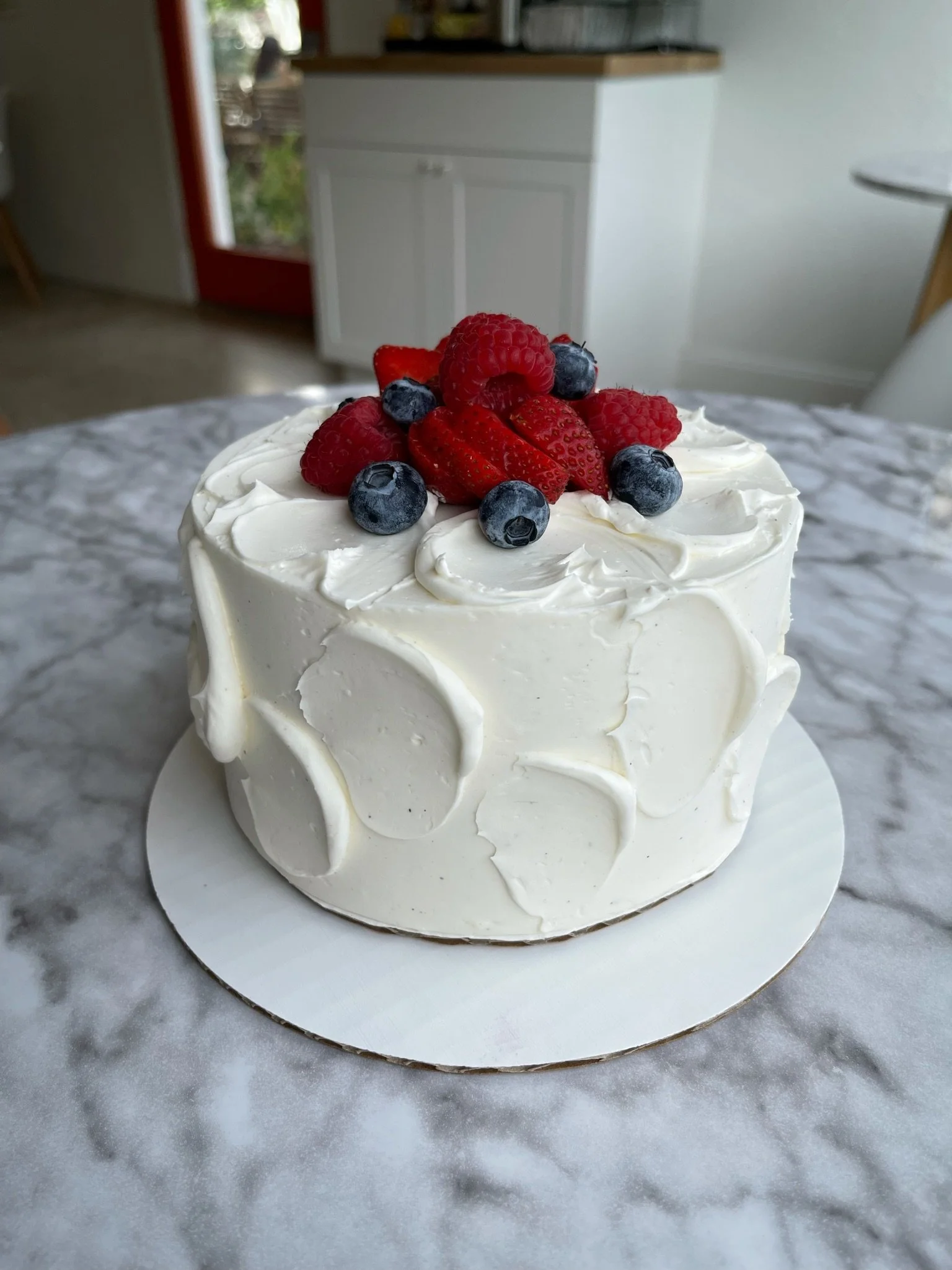 Vanilla cake with white icing and strawberries and blueberries on a marble table