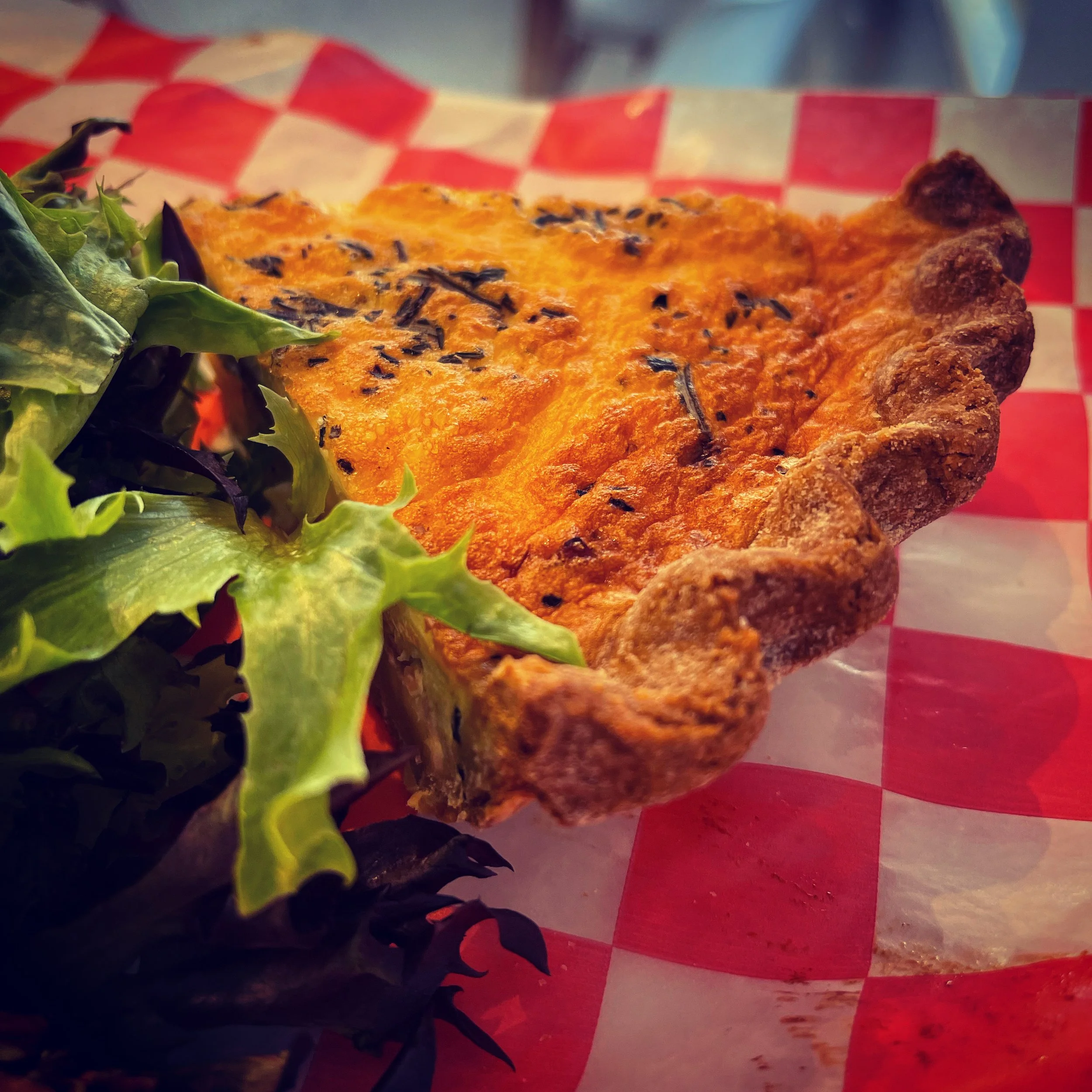 A slice of quiche pie with greens on red check paper