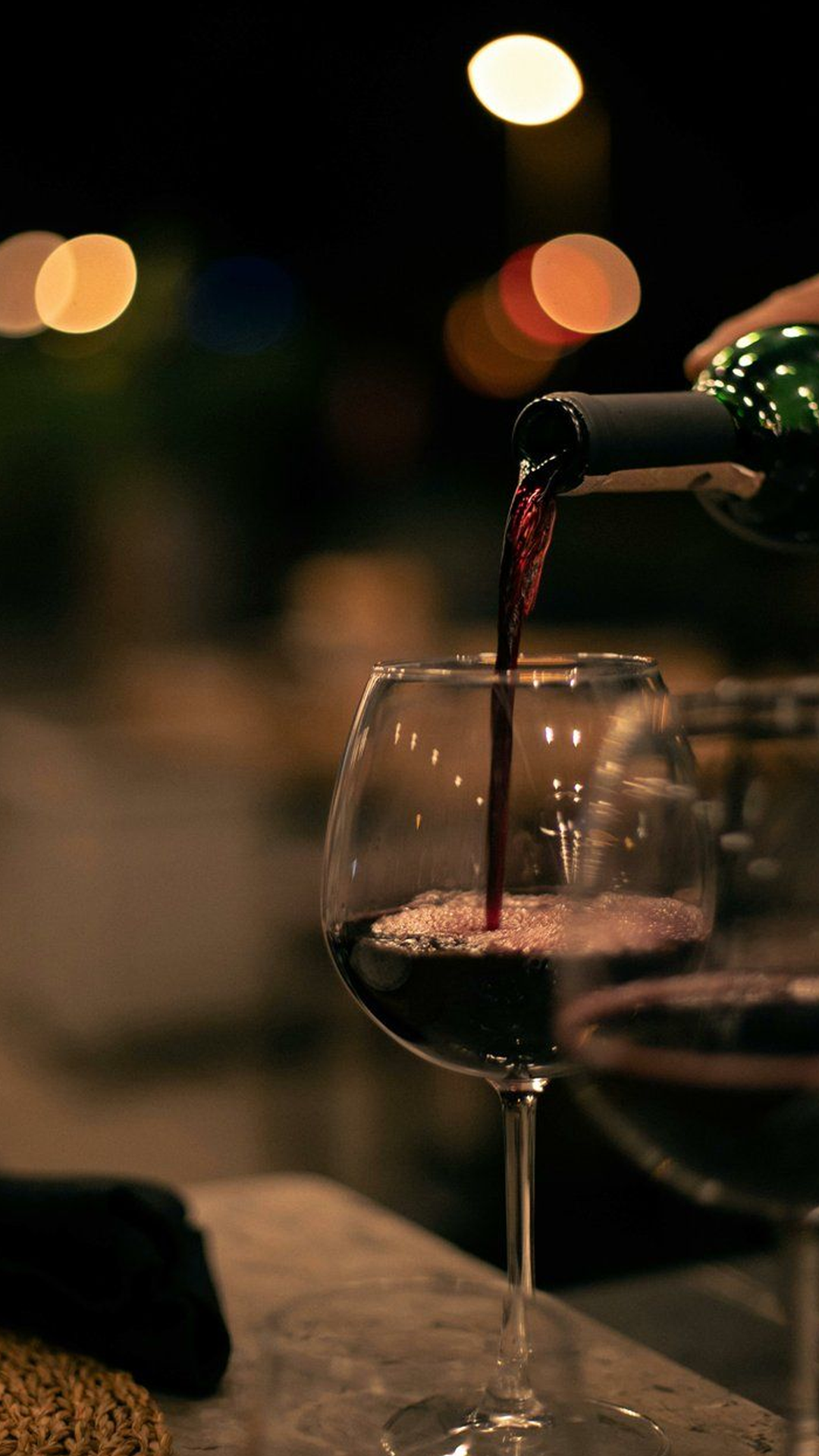 Red wine being poured into a glass at night, with blurred lights in the background.