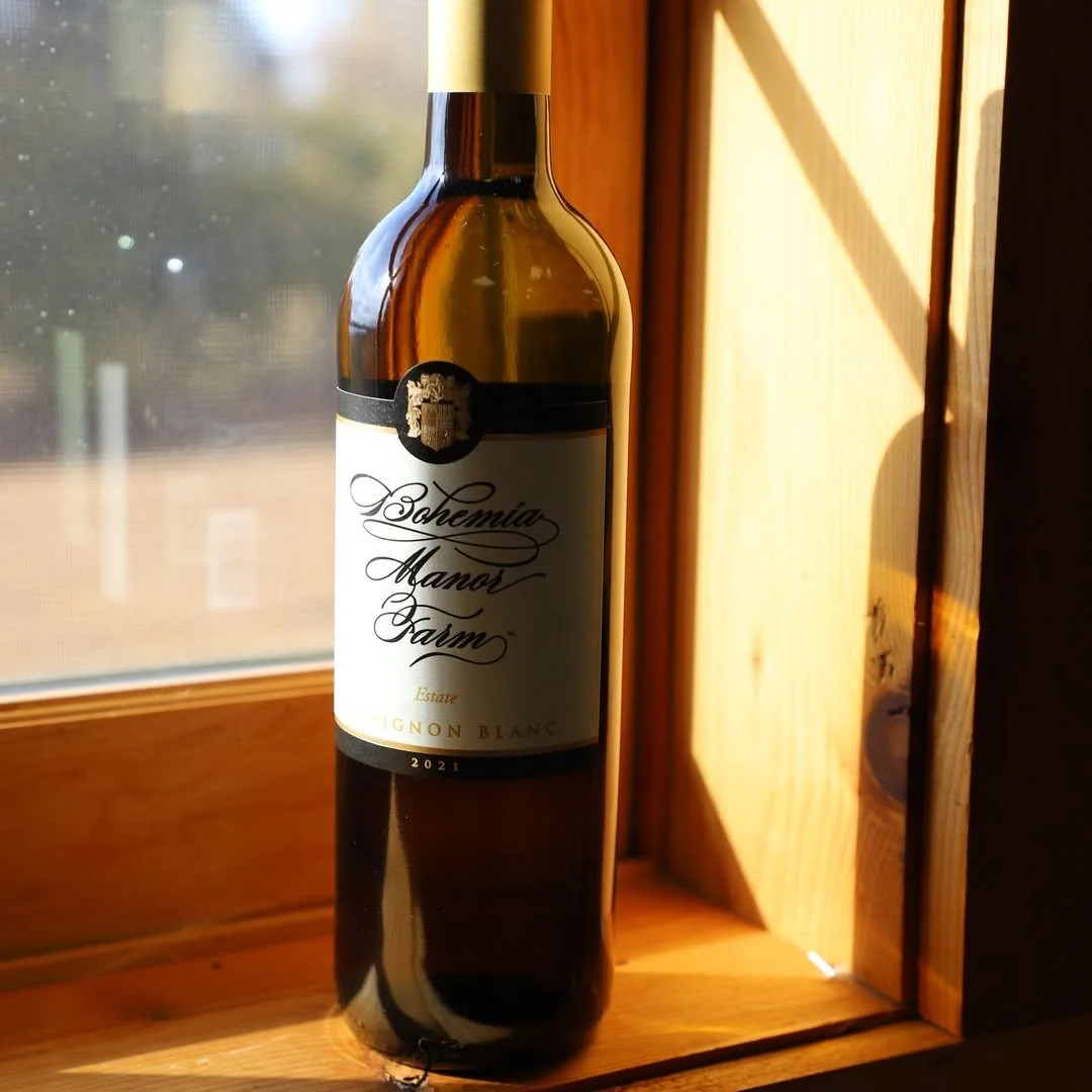 A bottle of Schoemia Manor Farm Sauvignon Blanc wine on a wooden windowsill with sunlight shining on it.